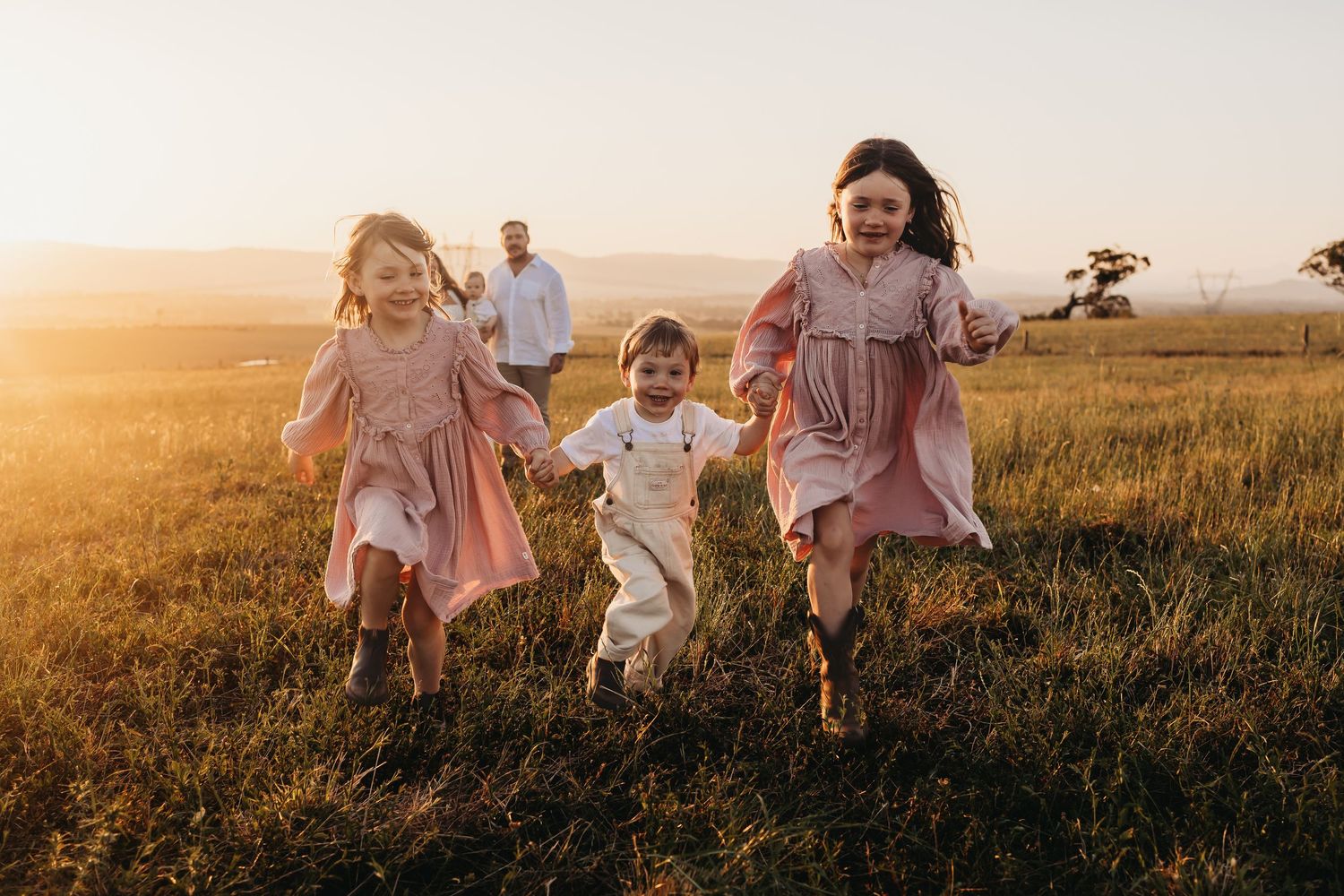 A family walks together through a golden wheat field at sunset while holding hands.