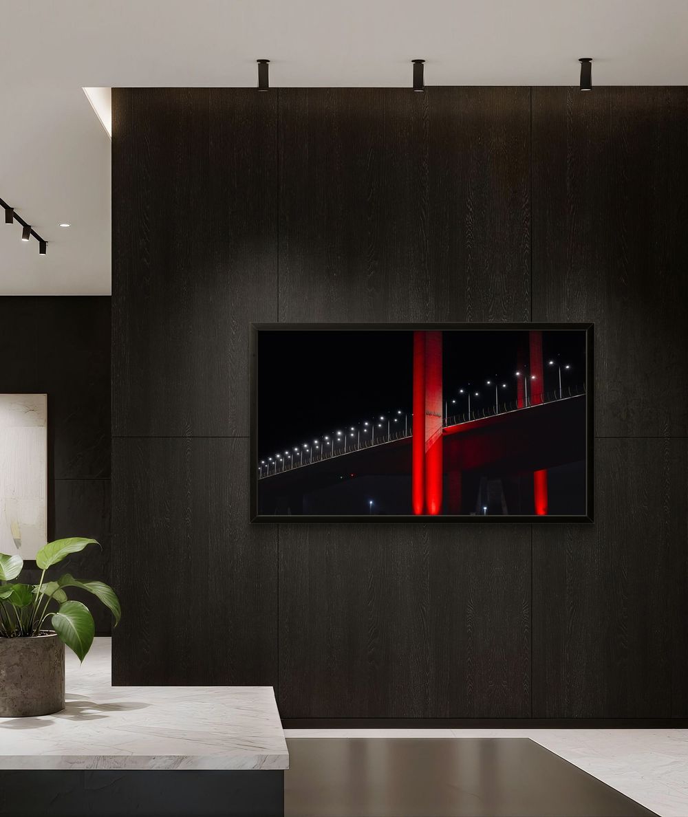 Framed fine art print of a red-lit bridge at night displayed on a dark feature wall in a lobby.