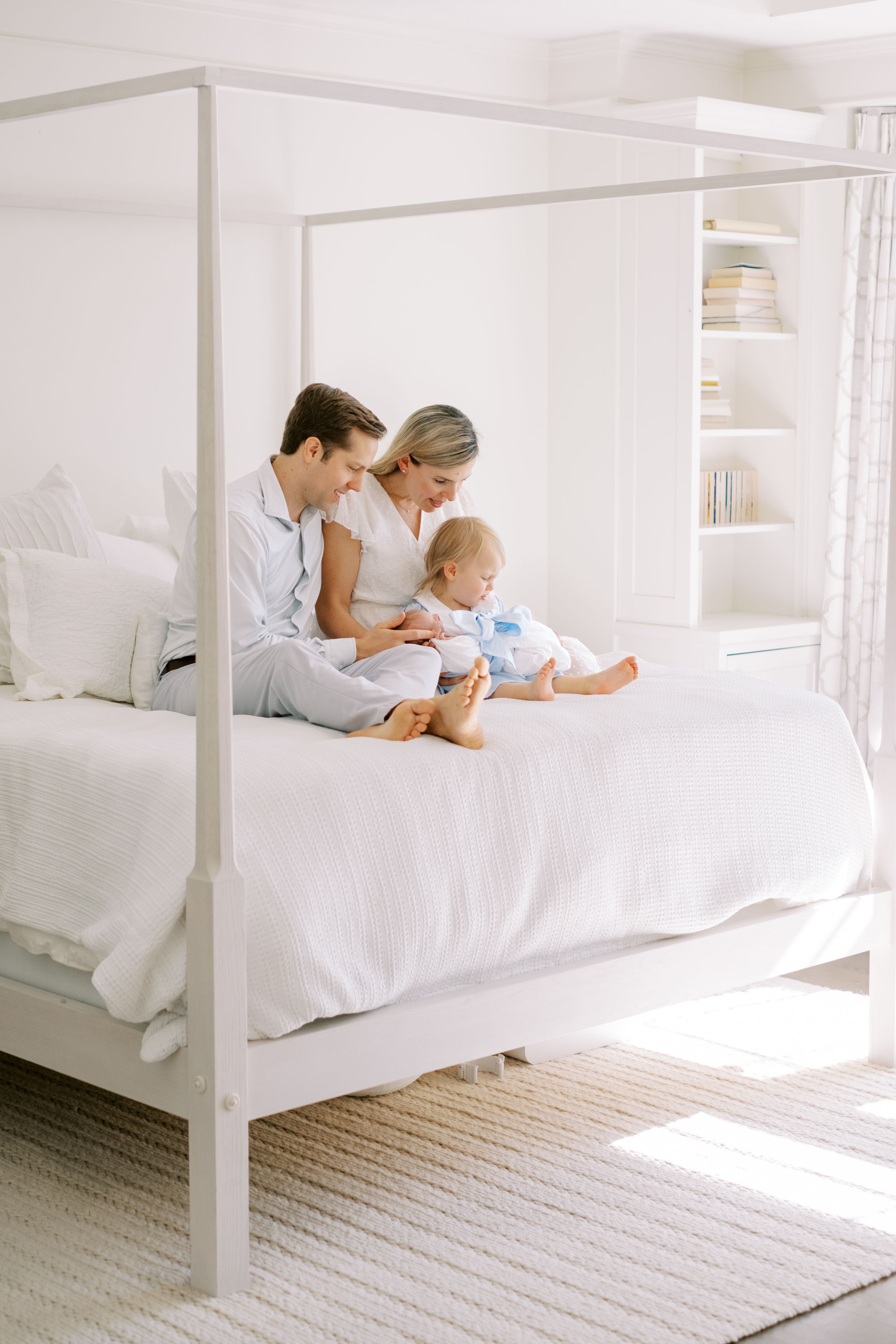 Family spending quality time together while relaxing on a white canopy bed in a bright, minimalist bedroom.