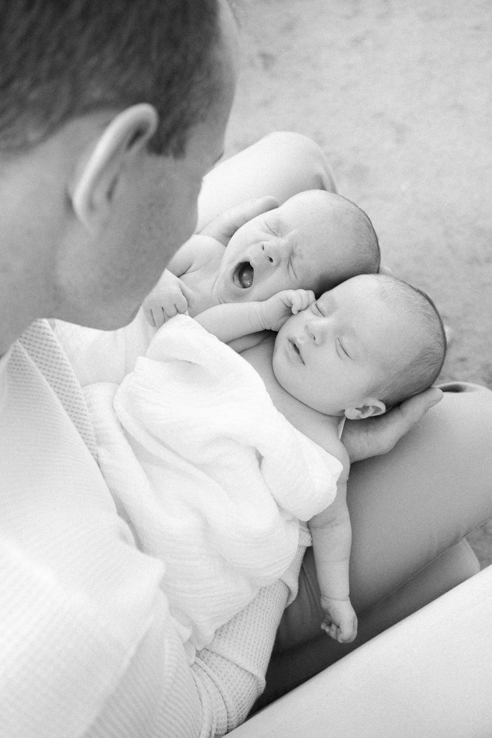 A series of black and white photos showing a baby in white clothing laying on their back in various peaceful poses.