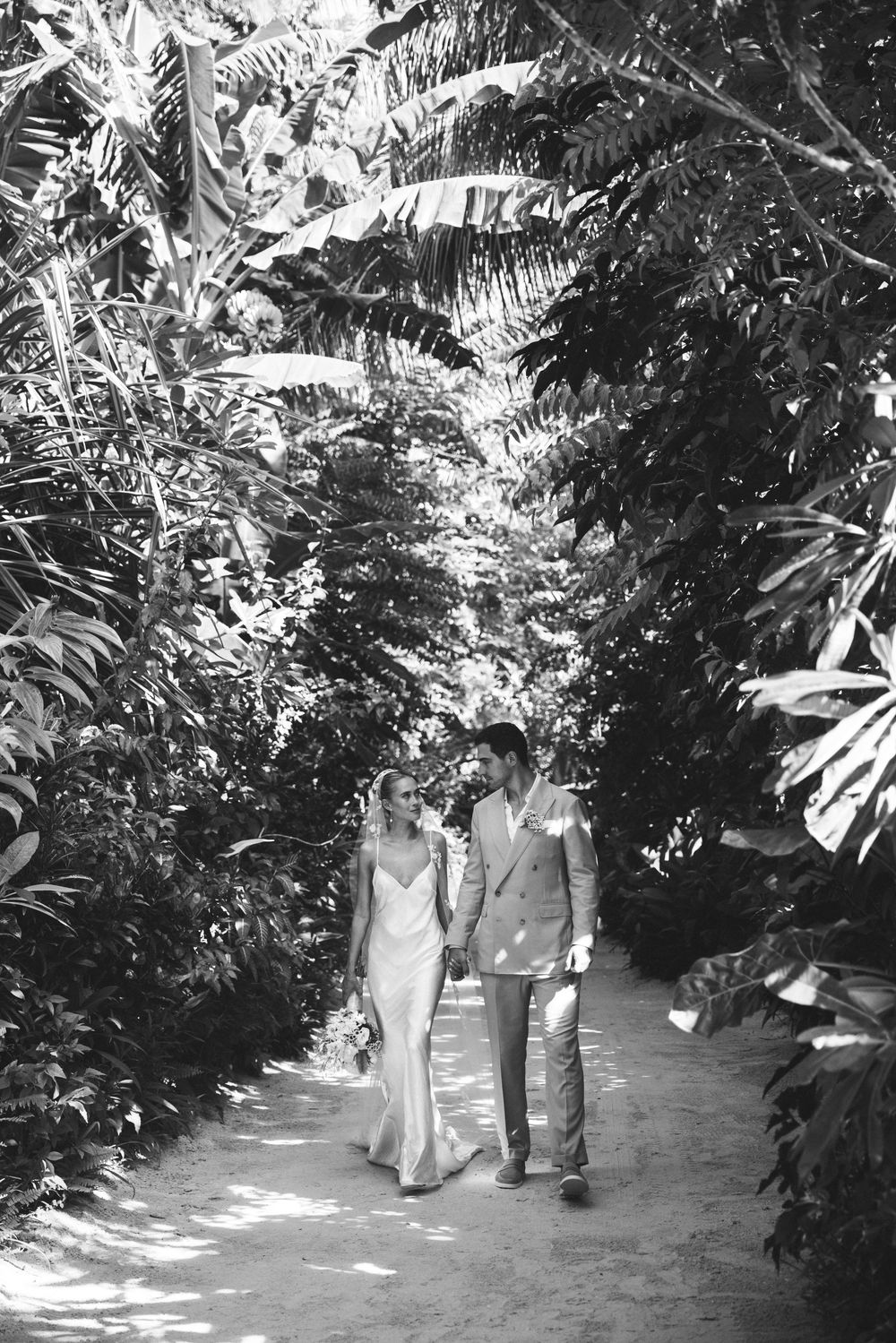 Couple walking through a sunlit tropical garden pathway.