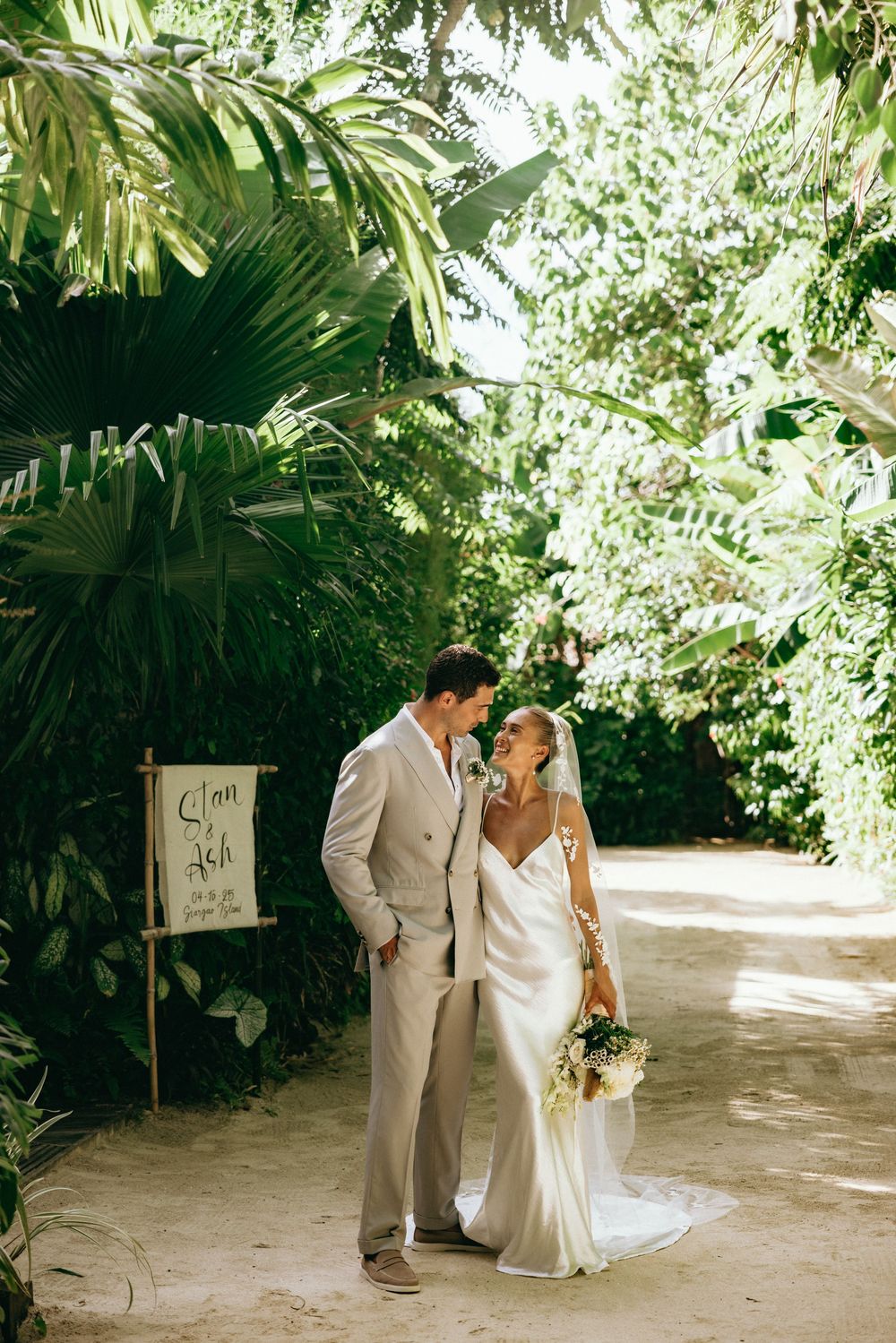 A couple shares a romantic moment on a tropical garden path during their wedding day.