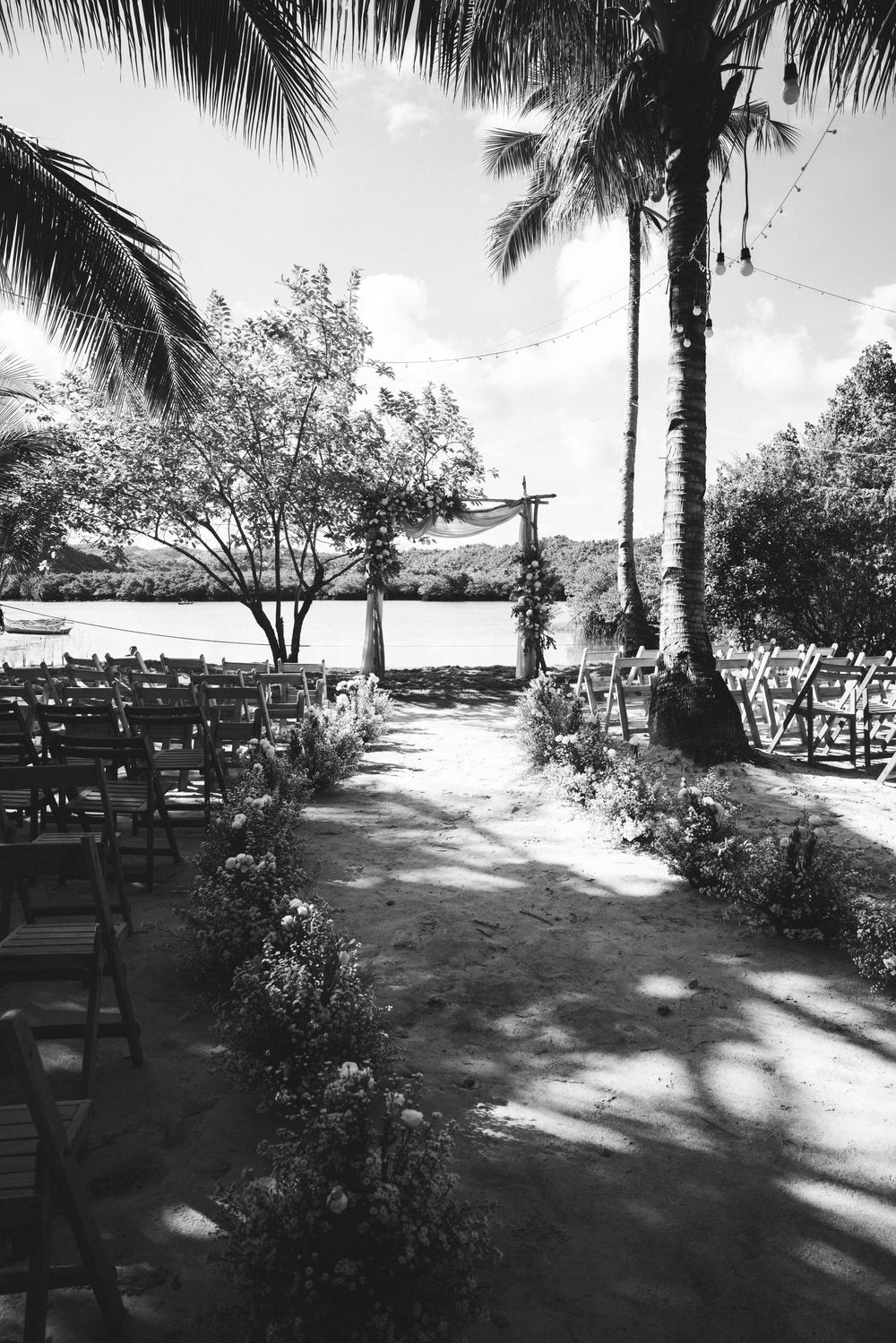 Black and white photo of an outdoor wedding venue with palm trees and rows of chairs.