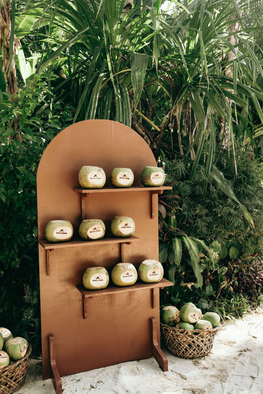 Brown wooden display shelf with decorative white pumpkins arranged in a tropical garden setting.