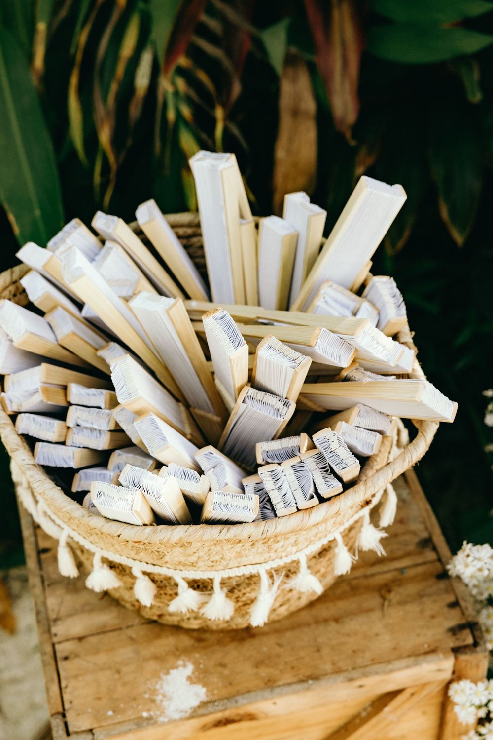 Basket filled with rolled paper wedding programs or favors on wooden surface.
