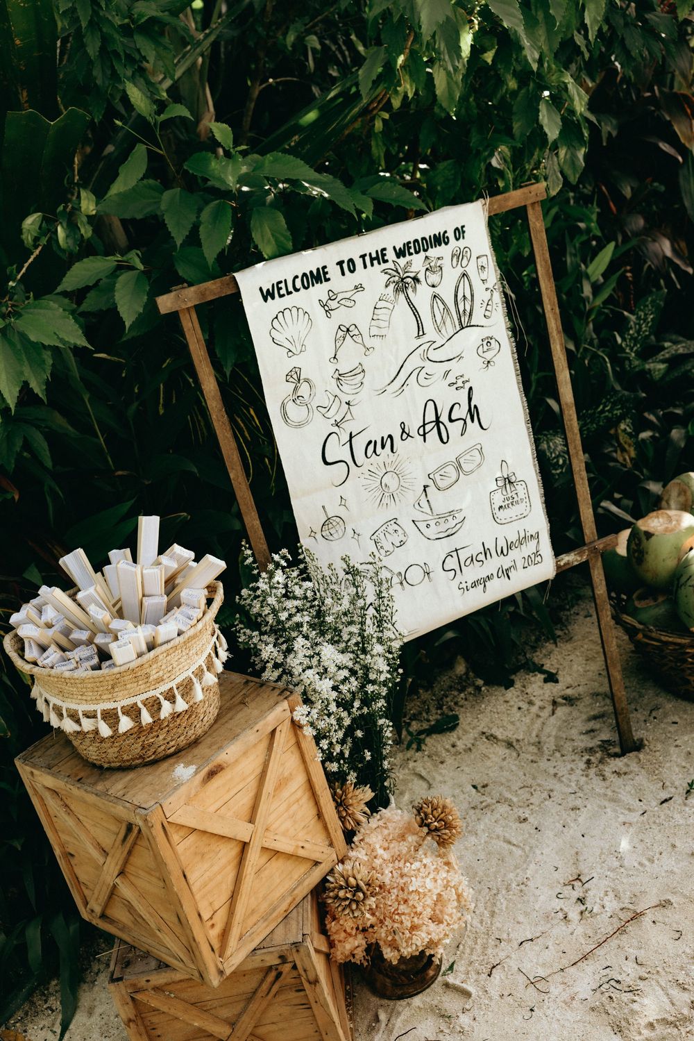 Wedding welcome sign and favor display with wooden crates in a garden setting.