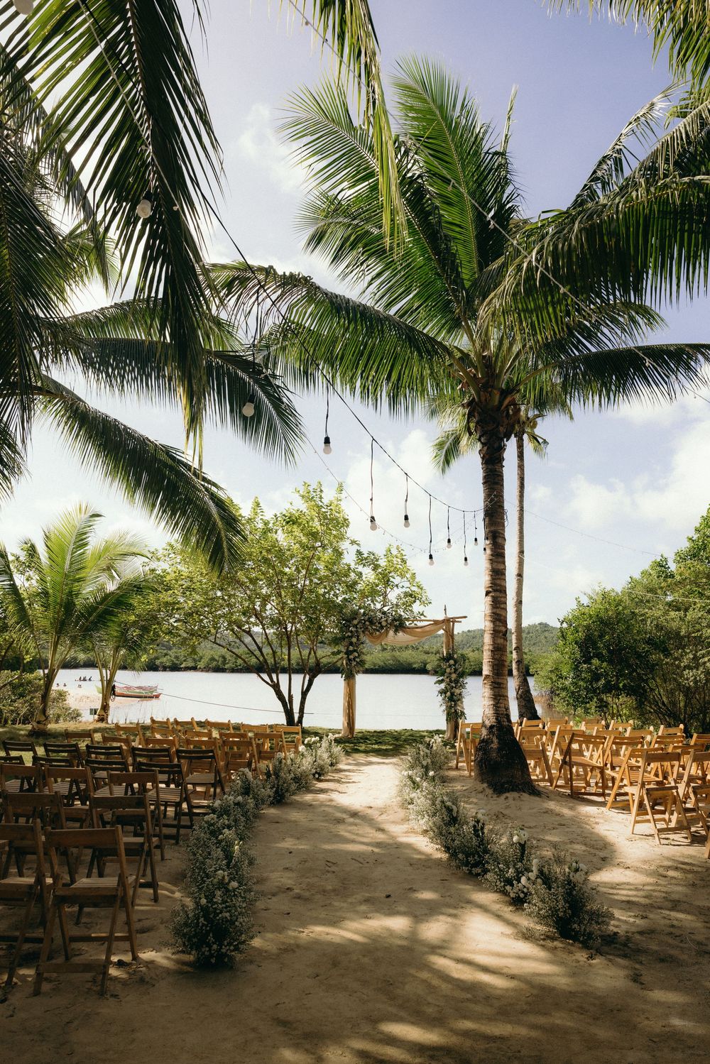 Rows of wooden chairs set up for a beach wedding ceremony under swaying palm trees with ocean views.