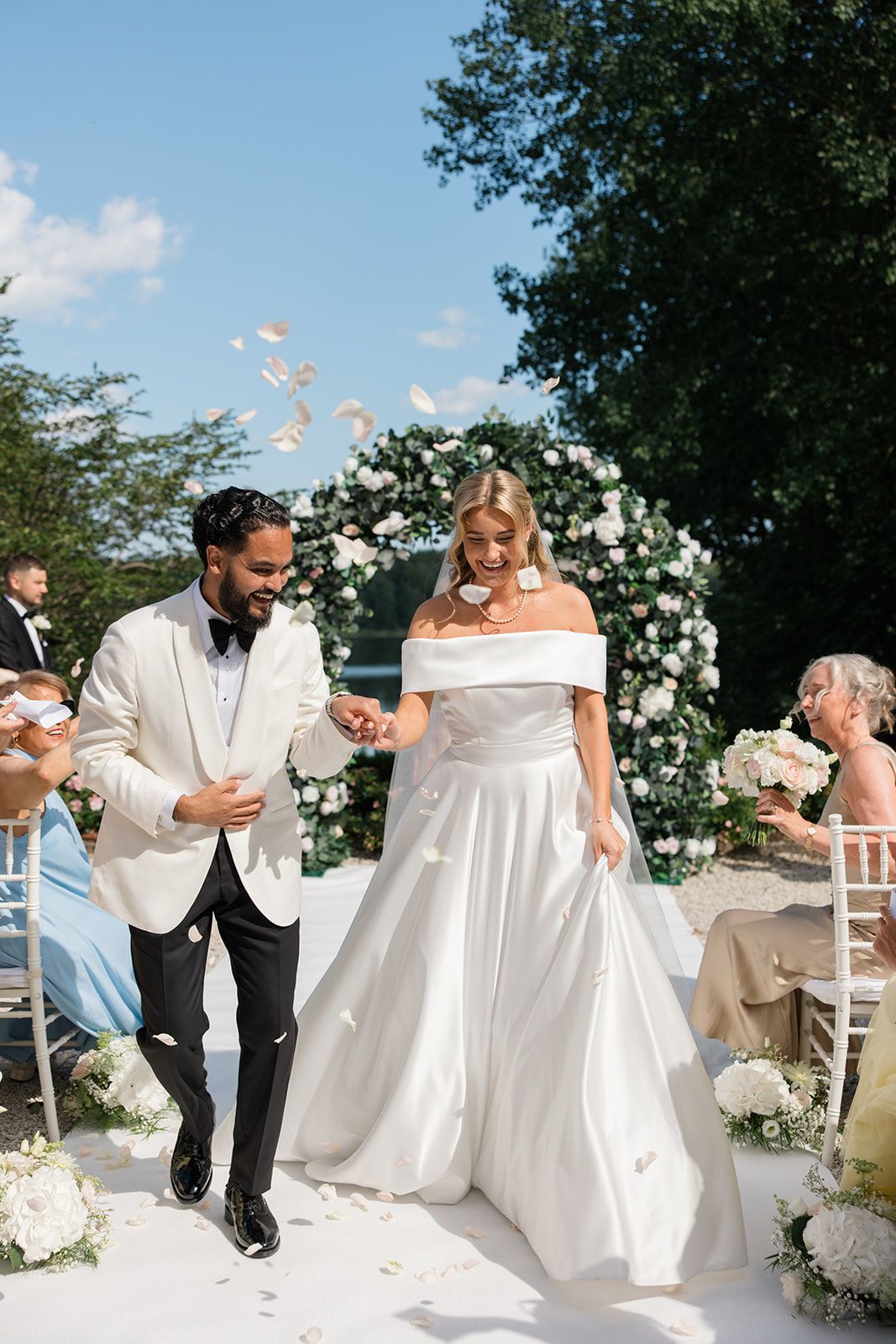 Wedding guests toss white flower petals during an outdoor ceremony celebration.