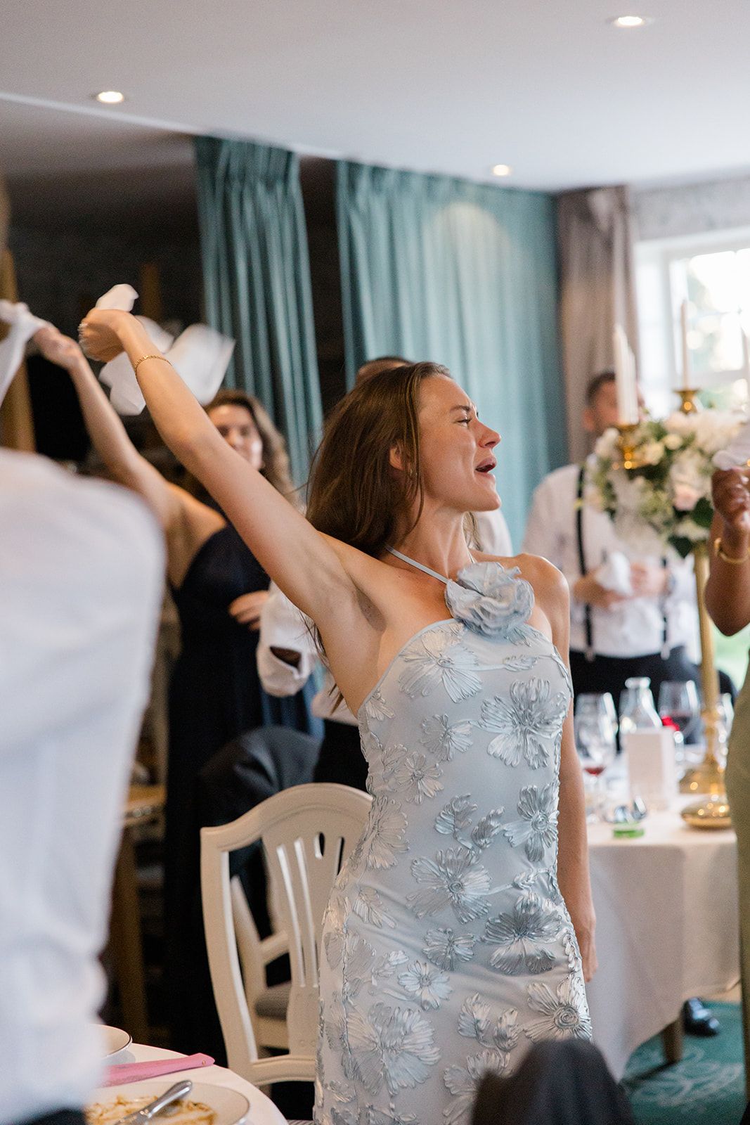 Wedding guest in silver dress shows excitement and joy while celebrating at an indoor reception venue.