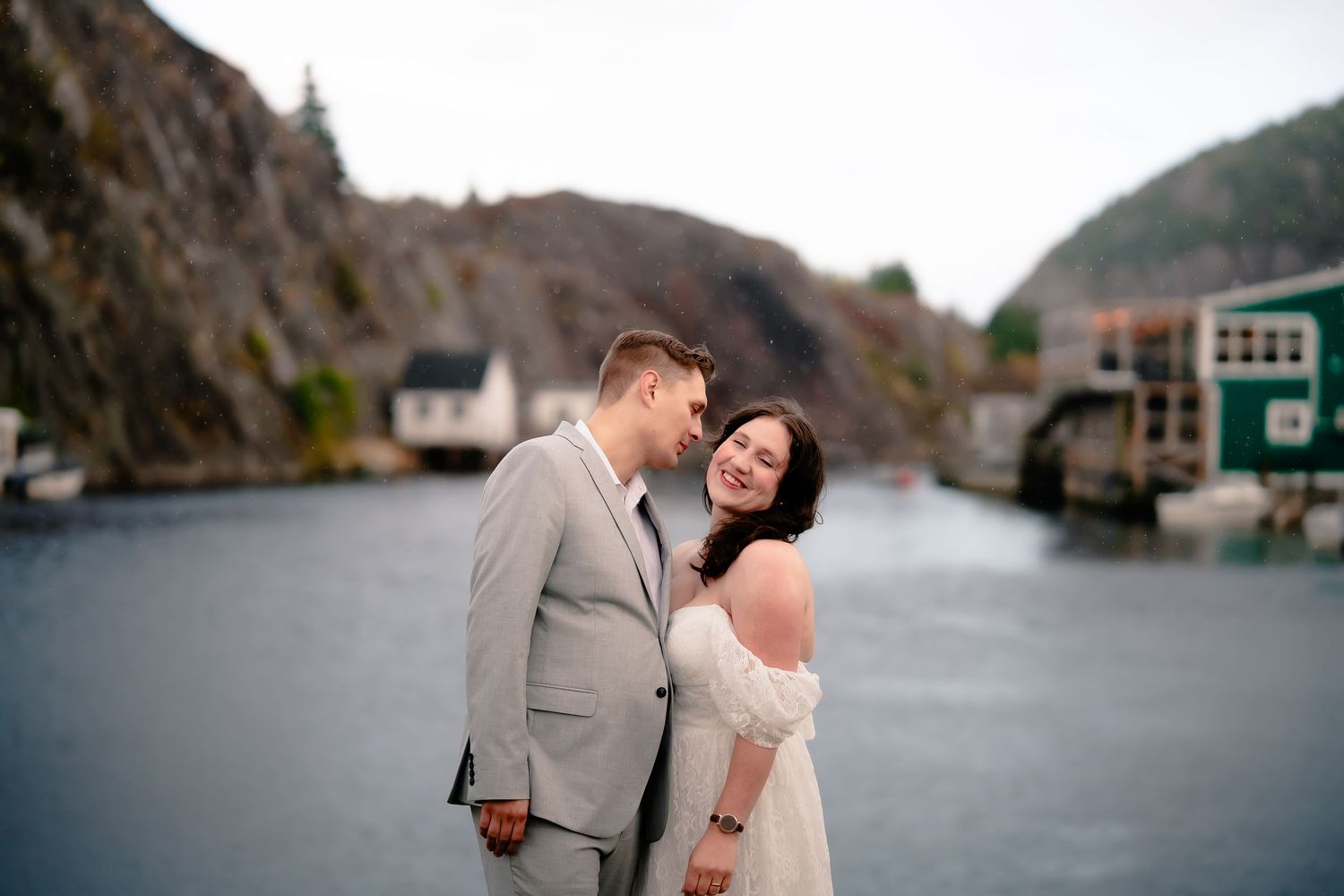 Newlywed couple in Quidi Vidi standing by the water with old Newfoundland houses in the background.