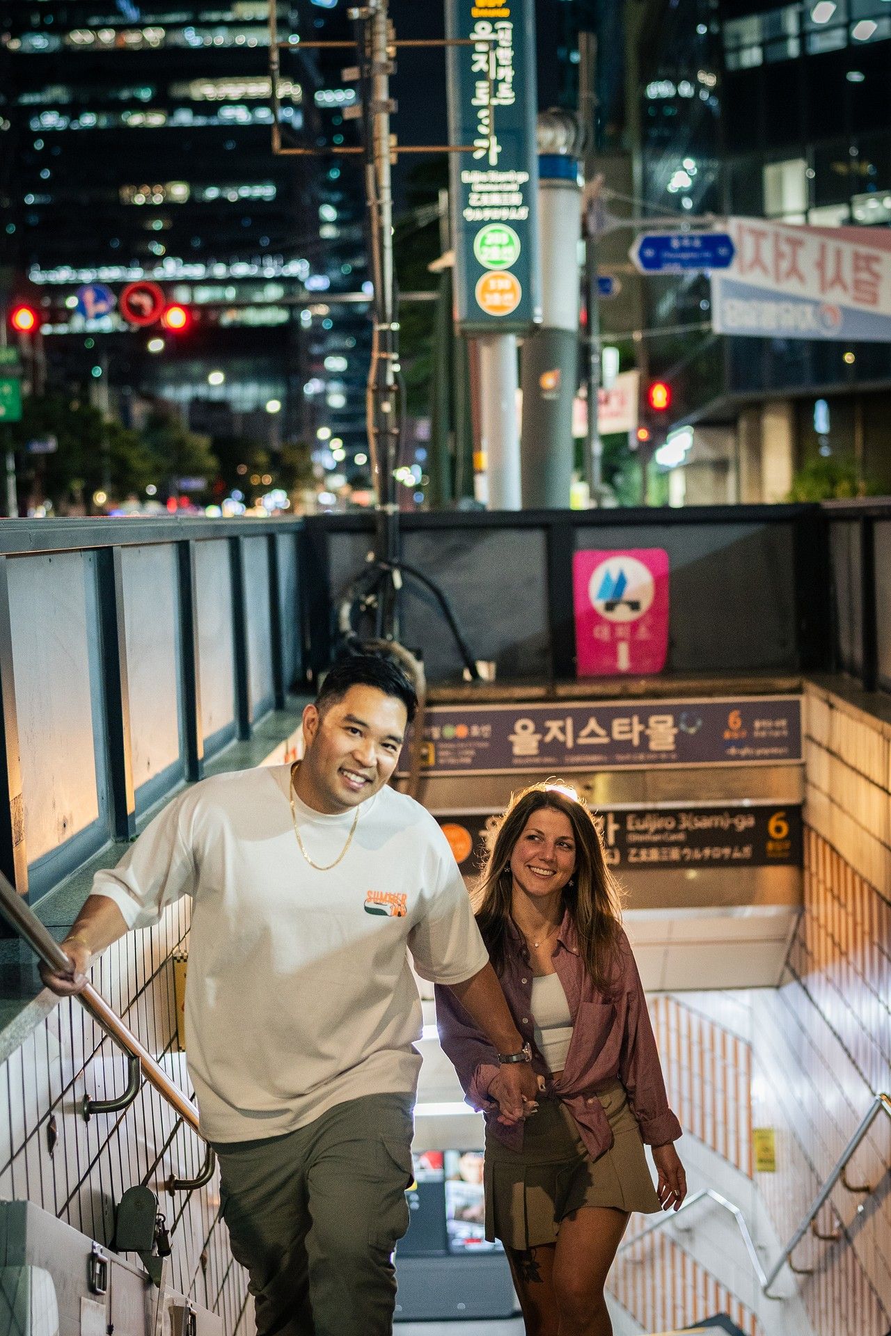 Couple walking up subway station stairs at night while smiling and laughing together in city setting.