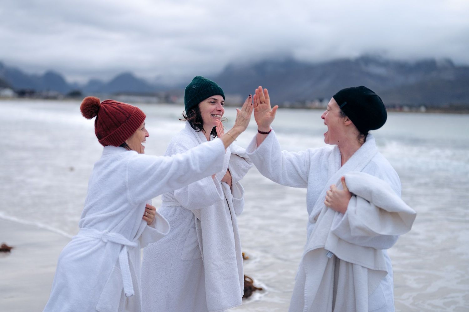 trois femmes en peignoir et bonnet qui se félicitent après leur baignade polaire sur la plage de rambergstranda