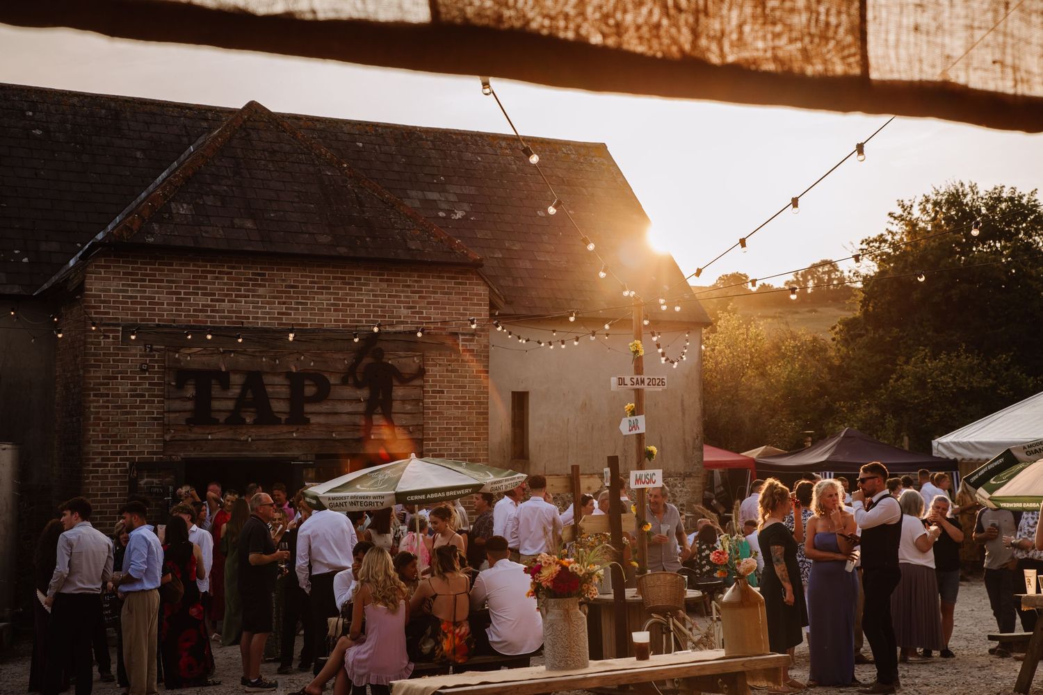 Dorset barn wedding venue at Cerne Abbas Brewery near Dorchester. Wedding guests enjoy golden hour from a candid Dorset Wedding Photographer