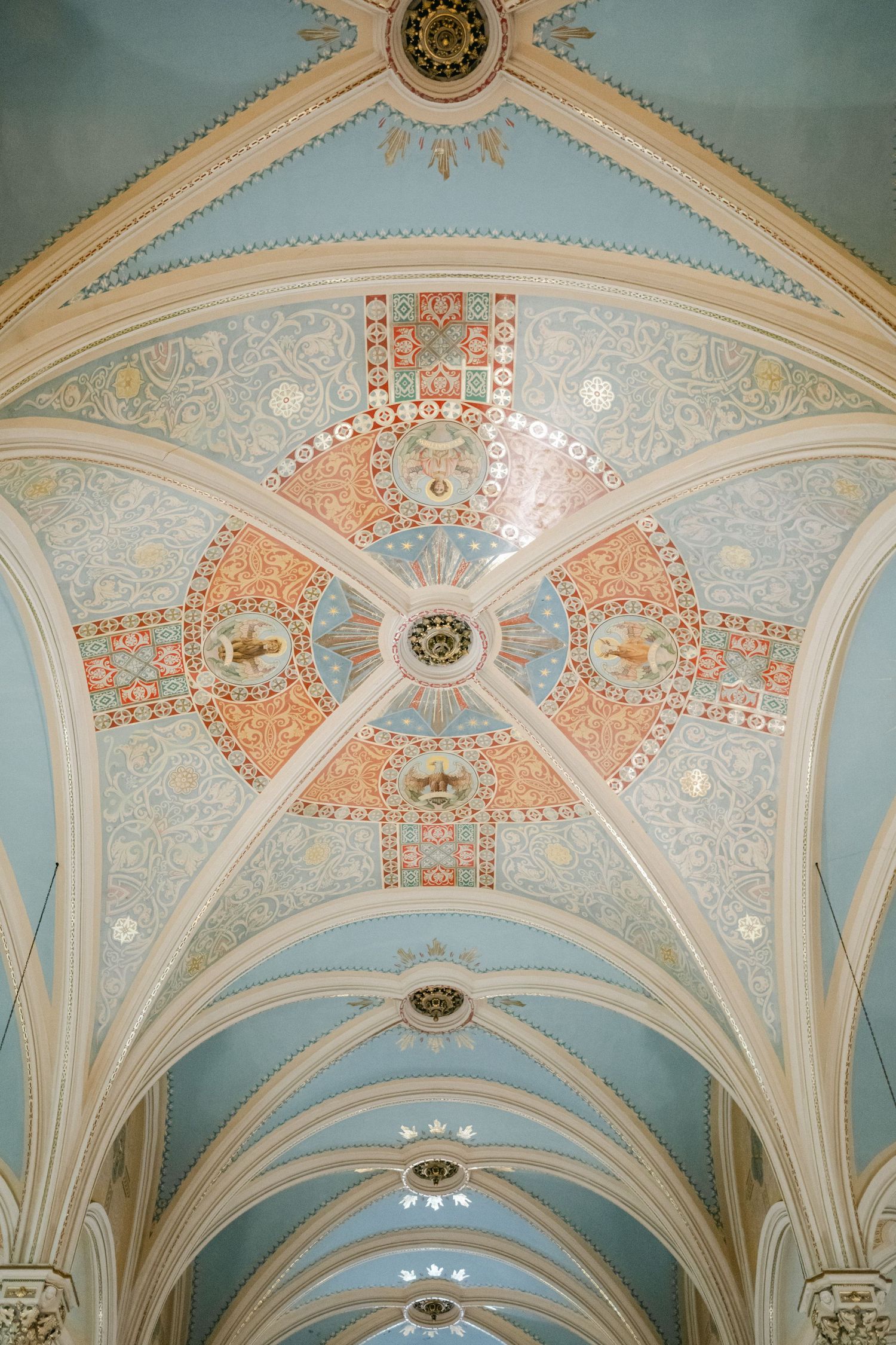 Ornate vaulted ceiling with pale blue and coral pink decorative patterns features elegant architectural details and chandeliers.