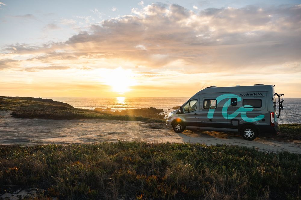 RV campers parked on coastal cliffs during golden hour with dramatic cloudy sky.
