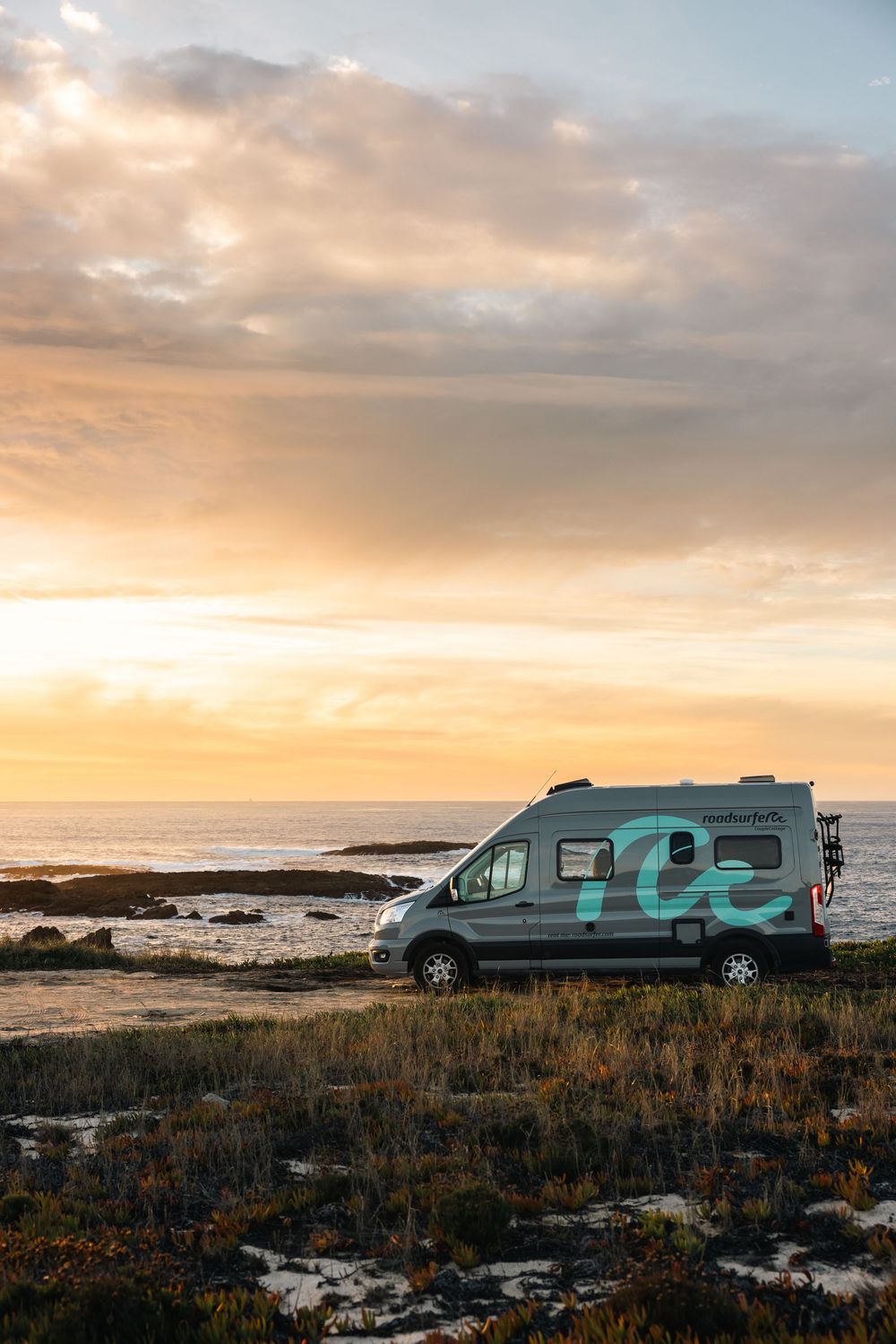 Two recreational vehicles camping on rugged oceanside terrain at sunset.