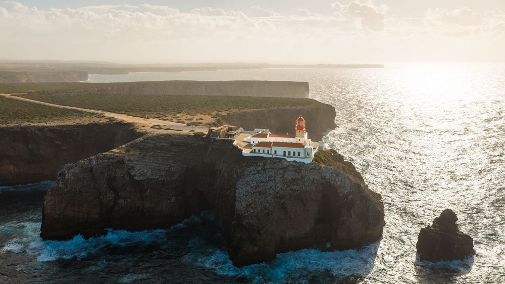 Dramatic coastal panorama at sunset showing cliffs and ocean waves meeting the shoreline.
