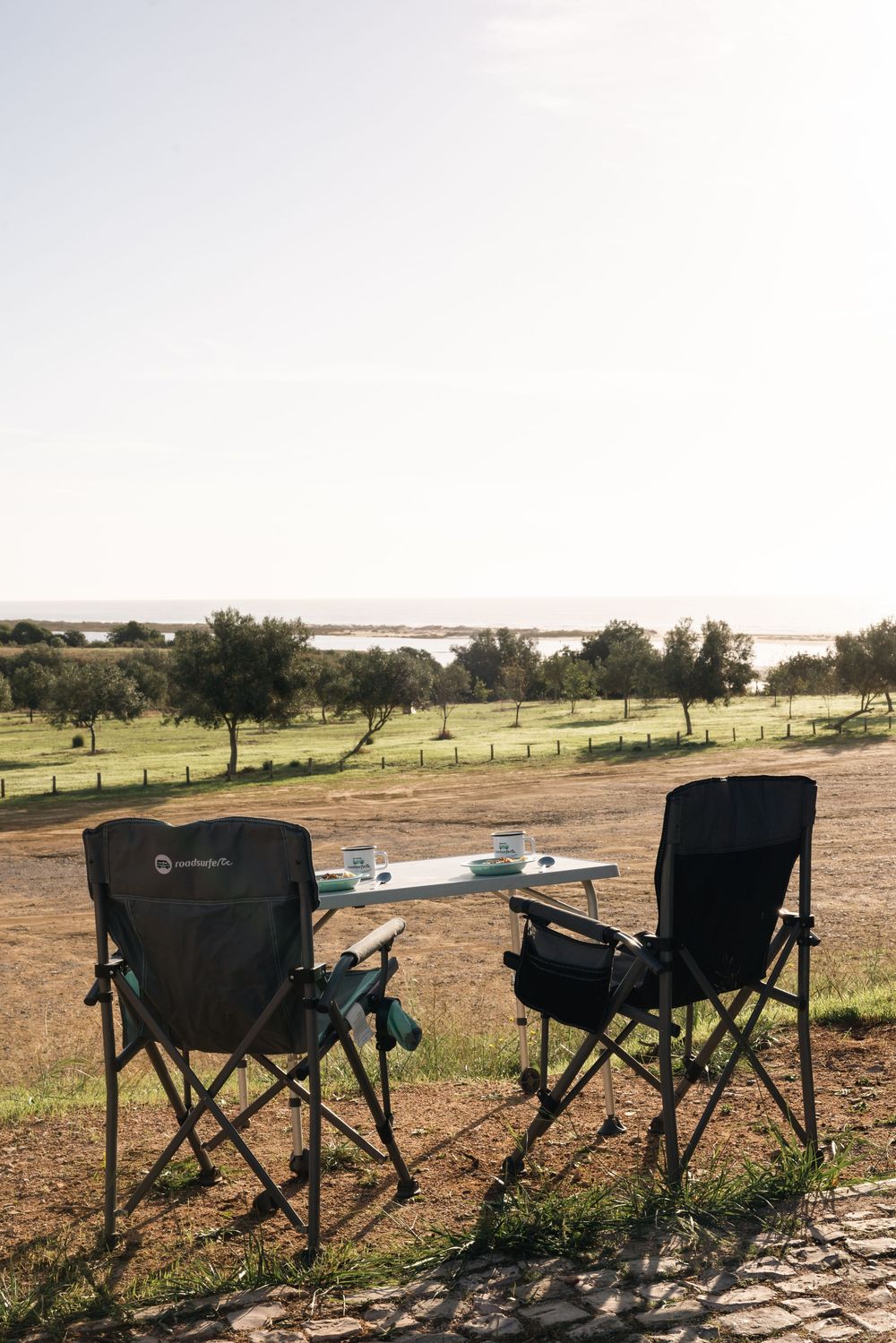 Row of camping chairs set up overlooking a scenic landscape with trees and fields.