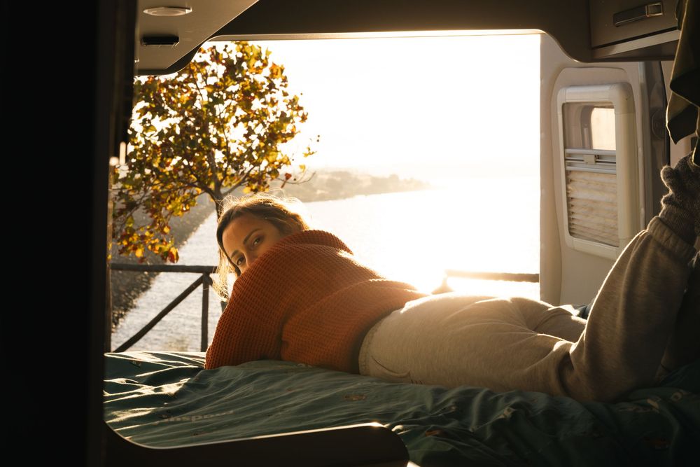 Cozy interior of camper van bed illuminated by warm sunset light.