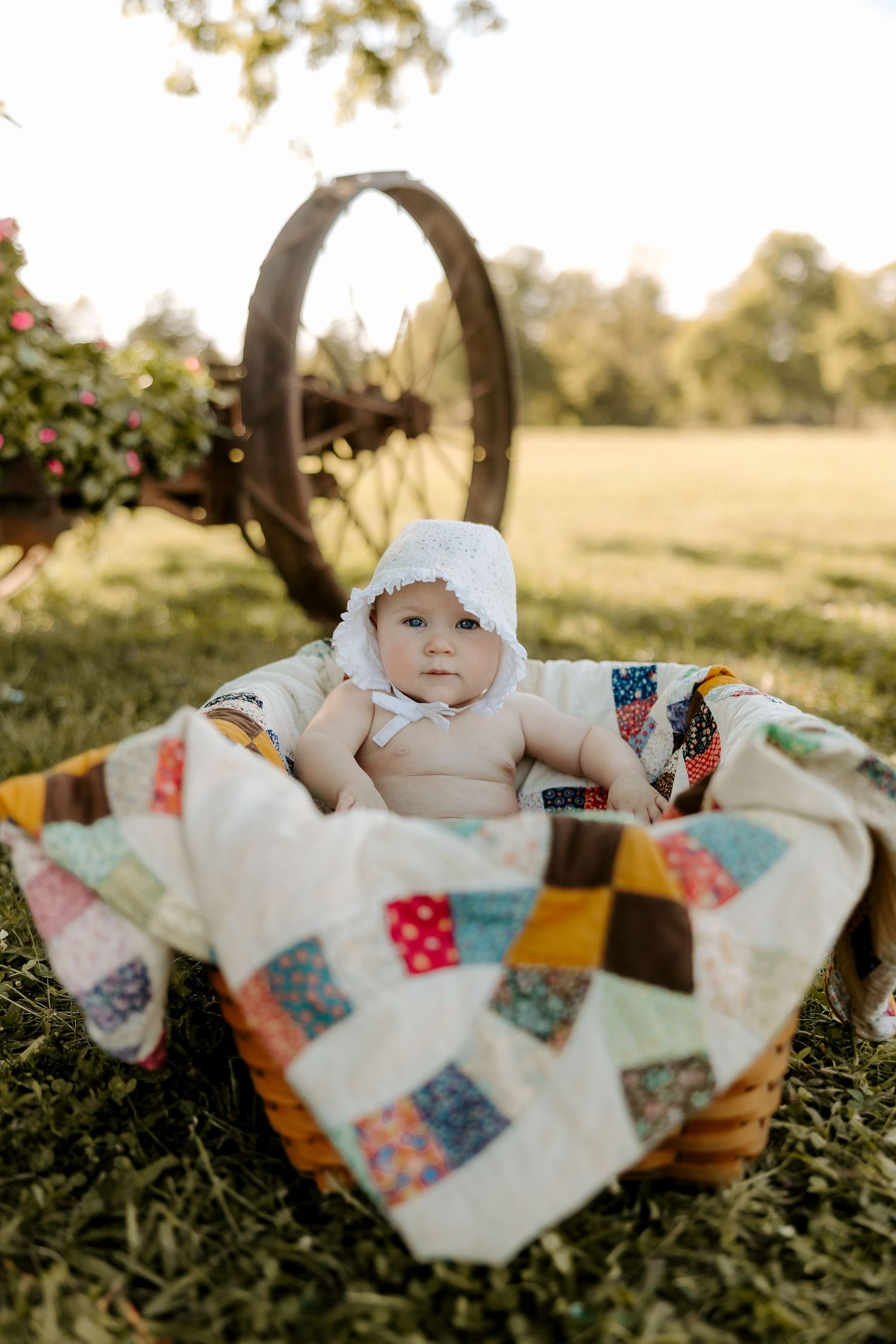 A woven basket with colorful patchwork quilt sits on grass in golden afternoon light.