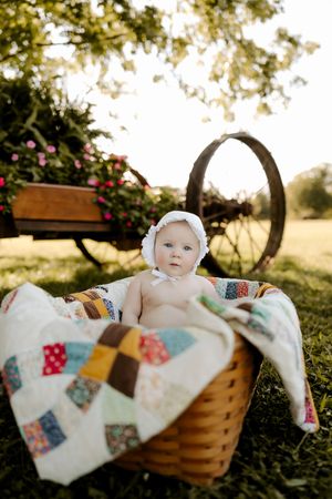 Outdoor photography setup with a decorative basket and colorful patchwork quilt under trees.