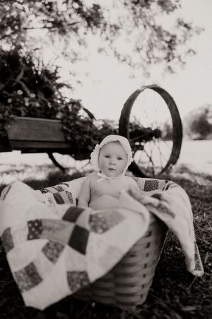 Black and white photo of a wicker basket with a handmade quilt outdoors.