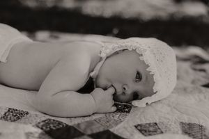 Black and white photo of baby in white dress lying on textured blanket.