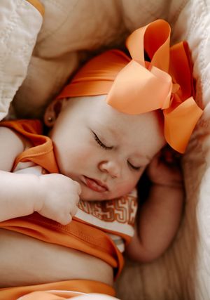 Close-up of sleeping baby in orange outfit with matching bow.