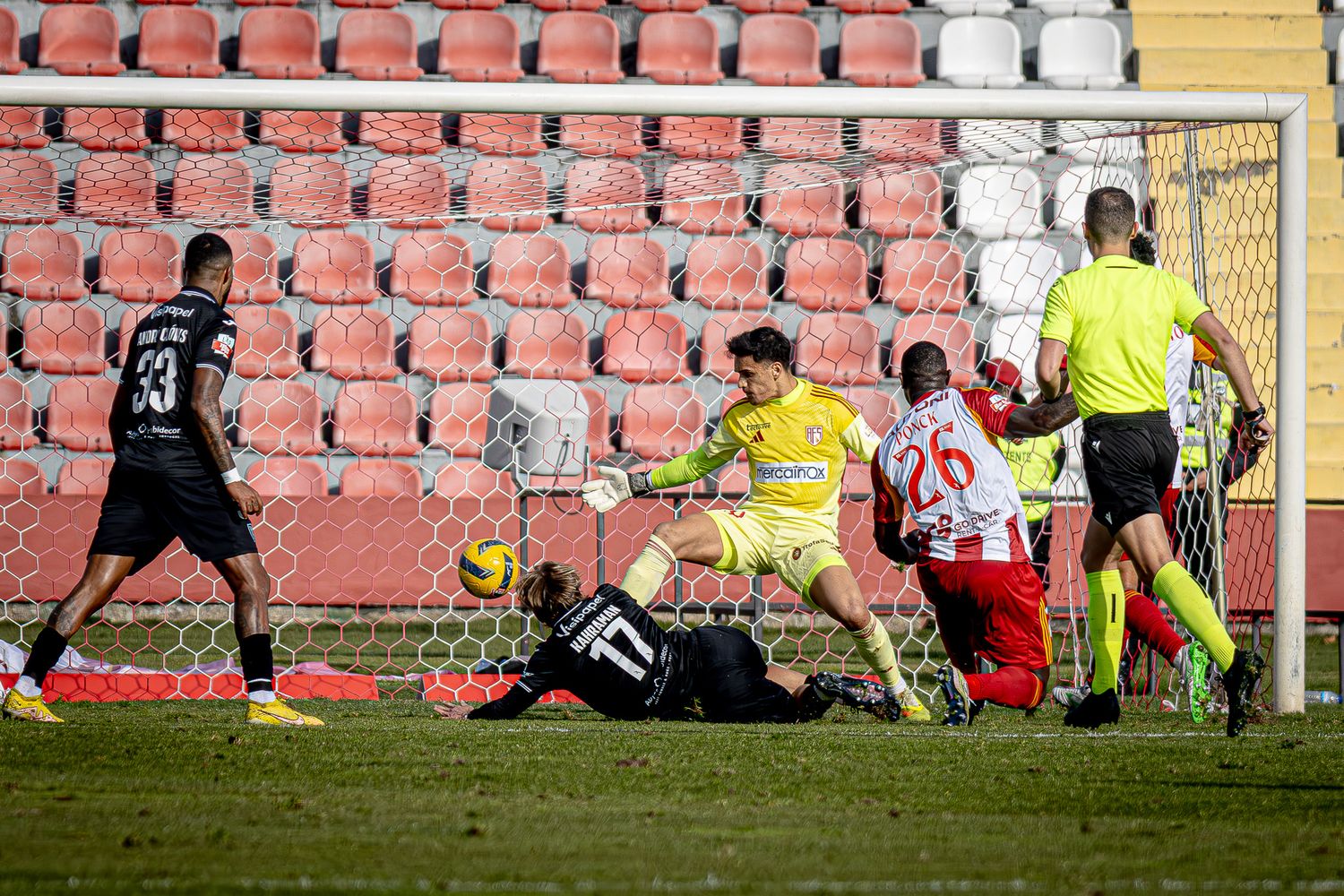 A dramatic goal-scoring attempt unfolds during a soccer match with players diving to defend.
