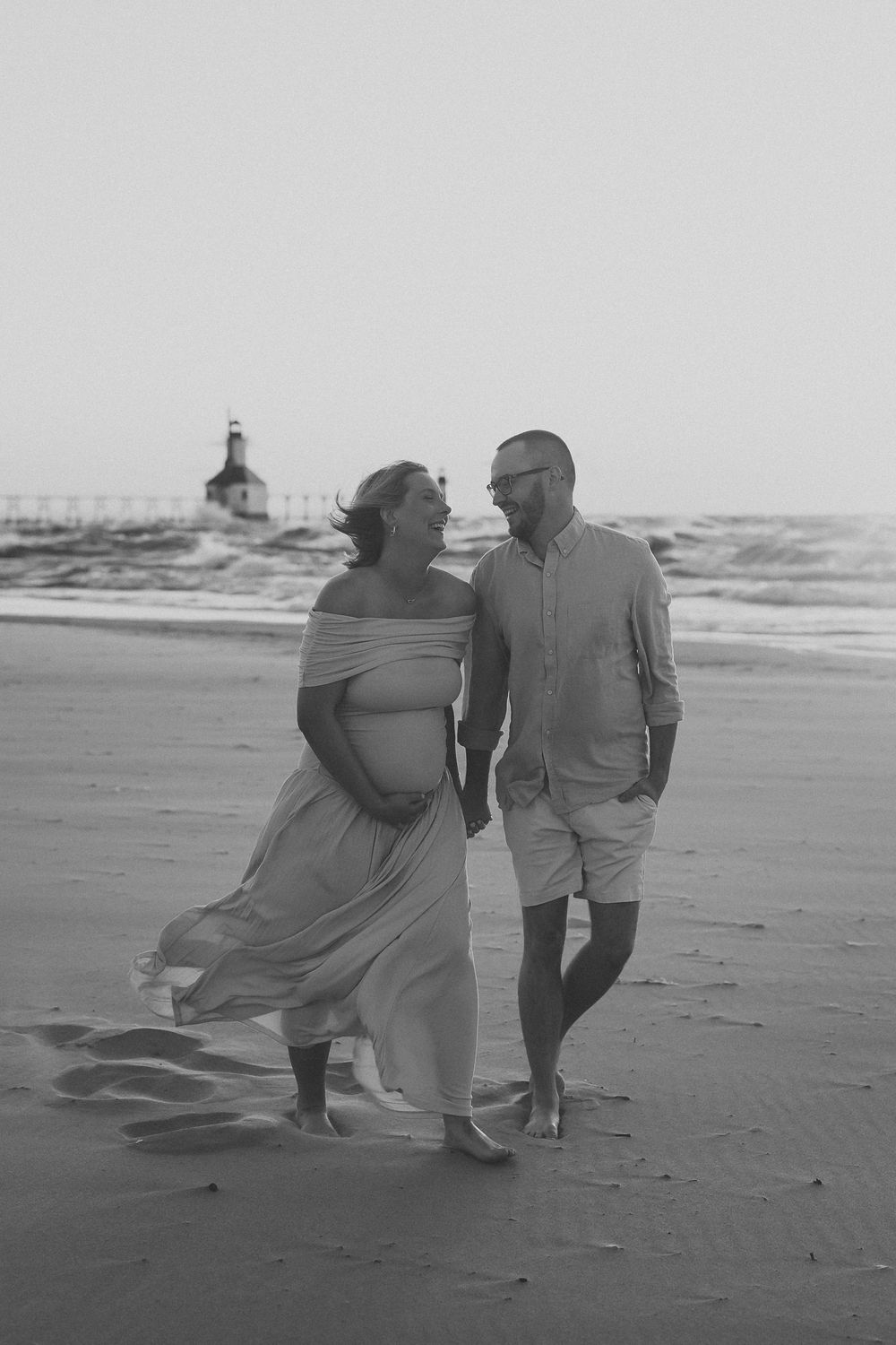 A couple walks together on a windy beach as her dress flows in the breeze in this black and white photo series.