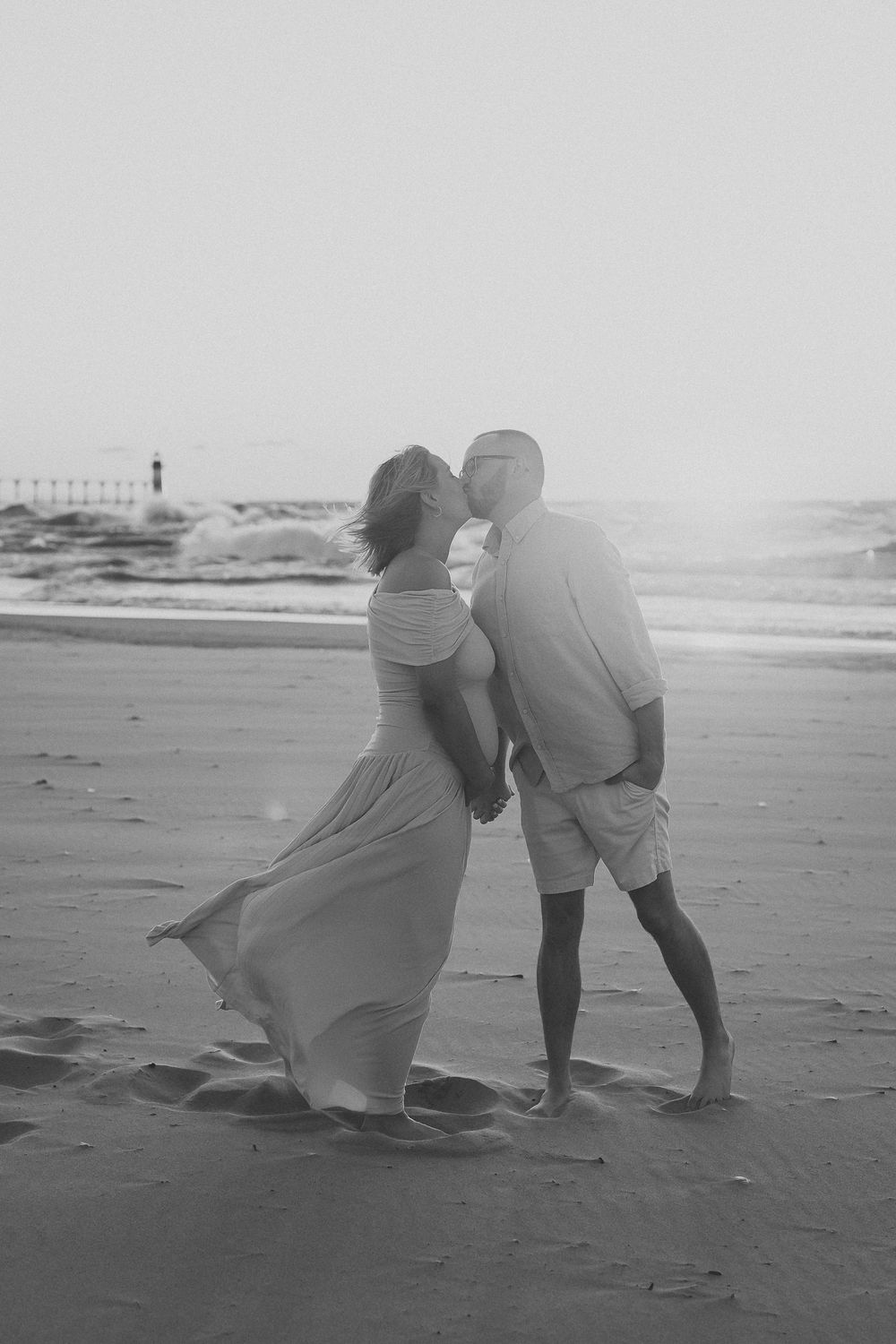 A couple playfully poses on a misty beach in black and white, creating artistic silhouettes in the sand.