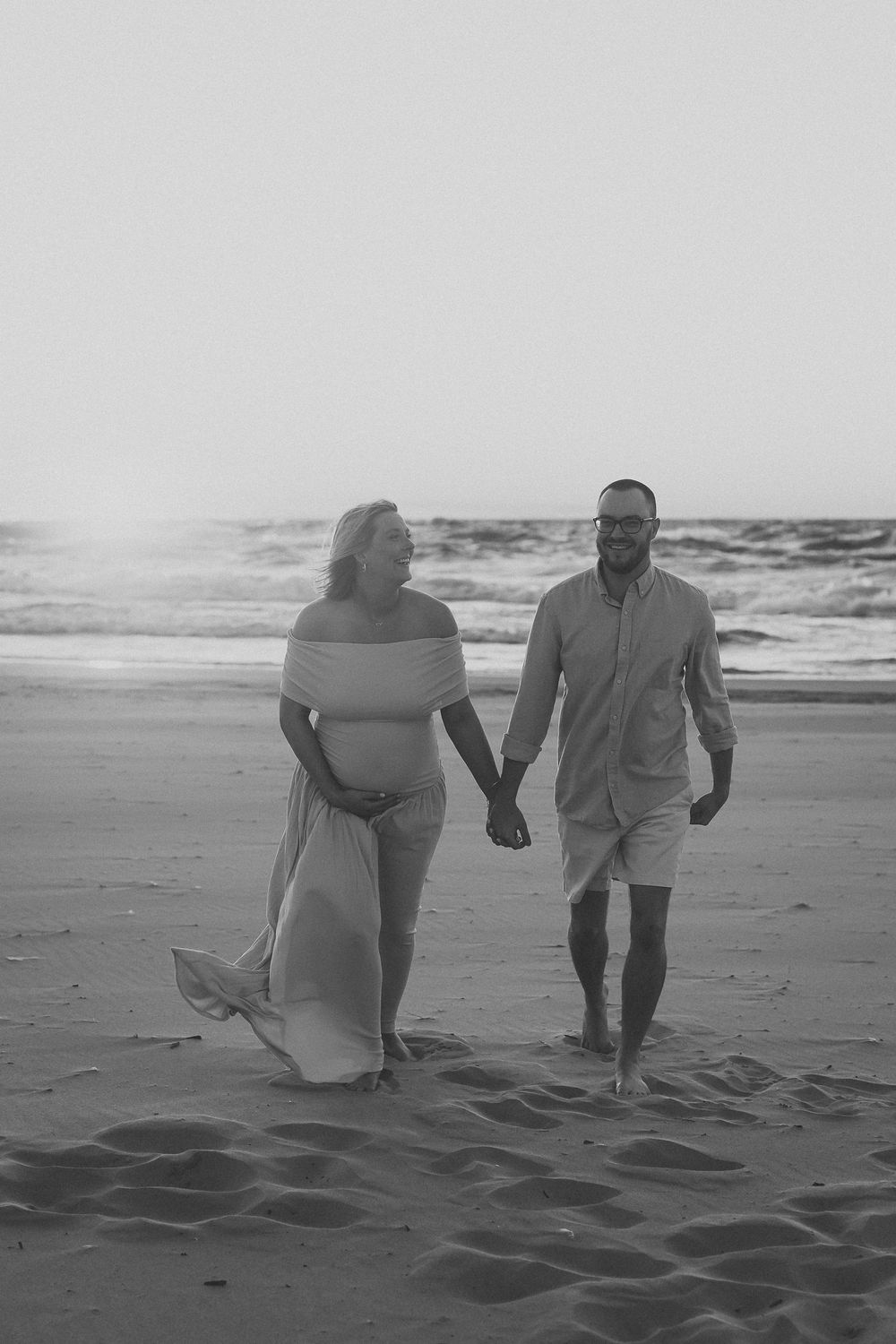 A couple shares a romantic moment on a sandy beach at sunset in black and white photography.