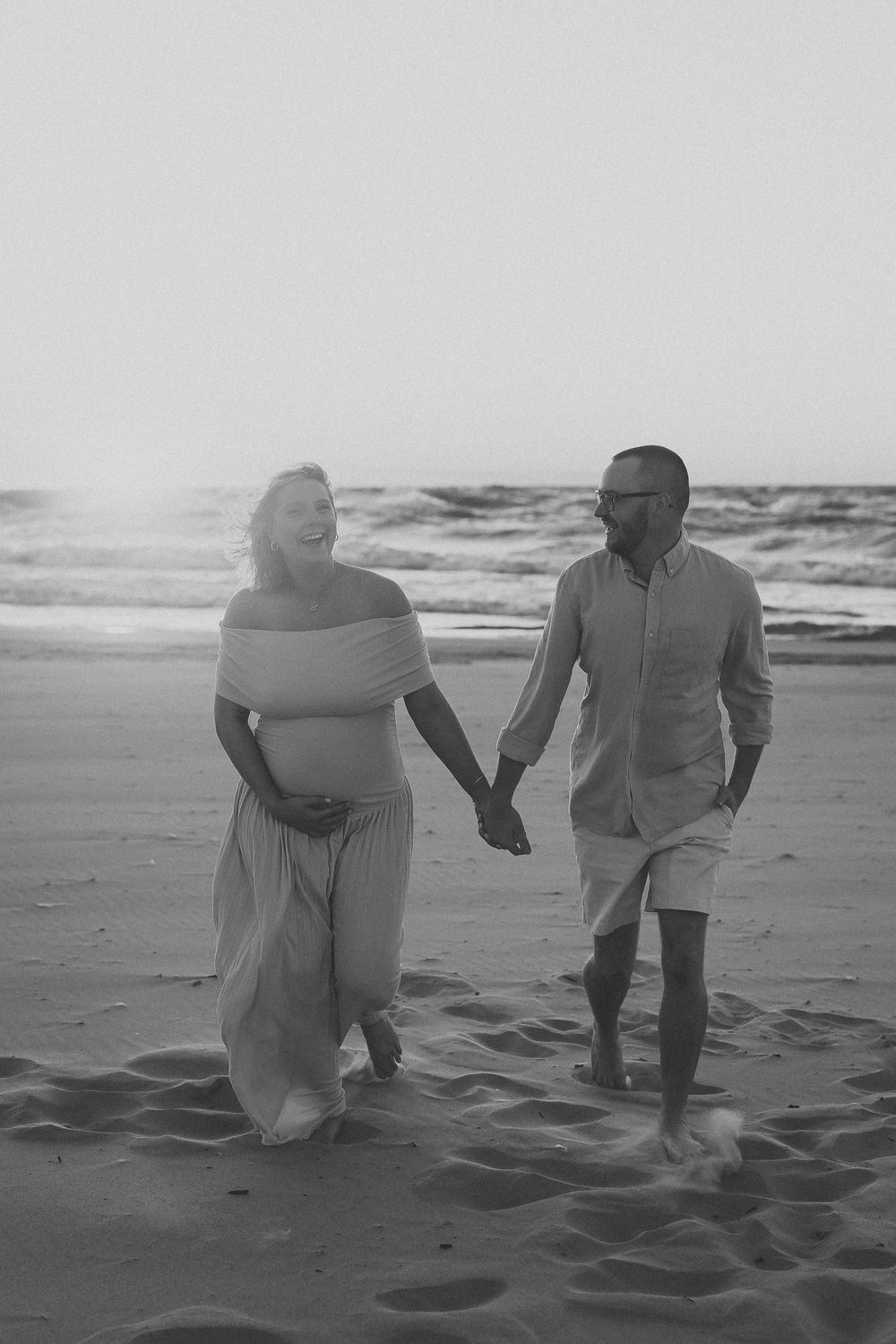 Black and white photo series showing a couple sitting and playing in the sand at a beach with ocean waves in background.