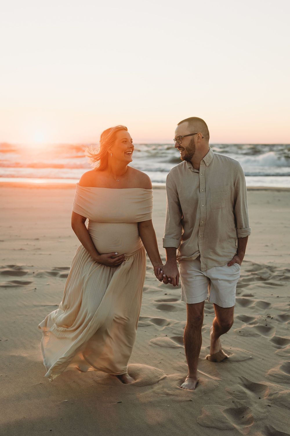 A couple walking hand in hand on a sandy beach at sunset, with waves crashing in the background.