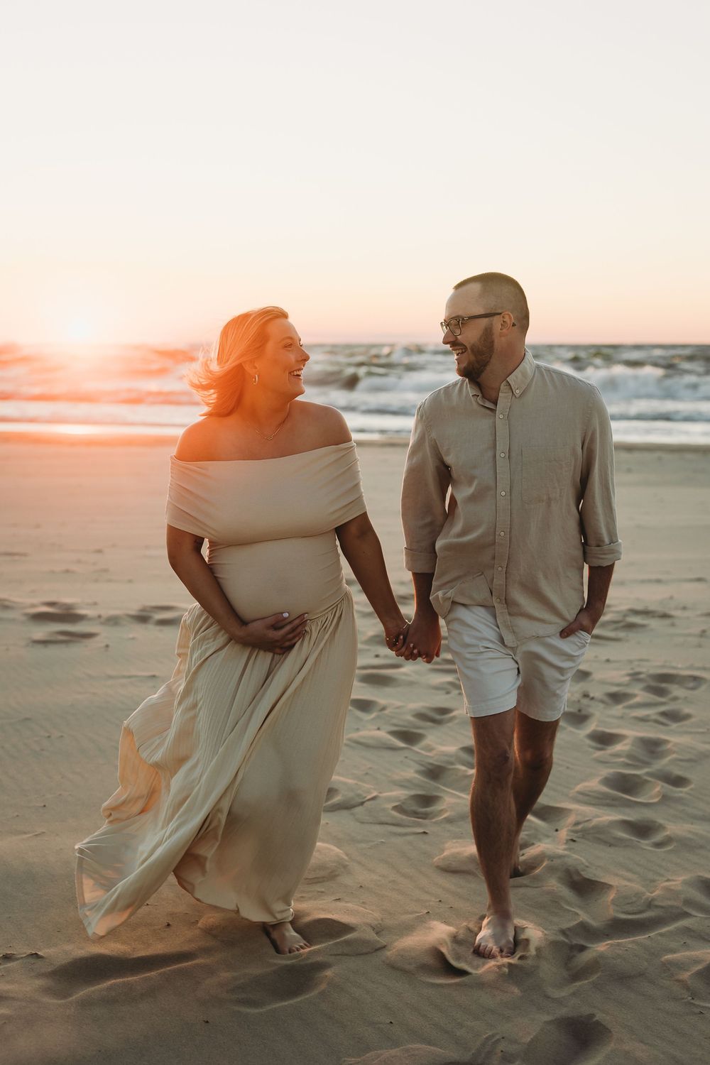 A couple walks along a sandy beach at sunset, creating romantic silhouettes against the orange sky.