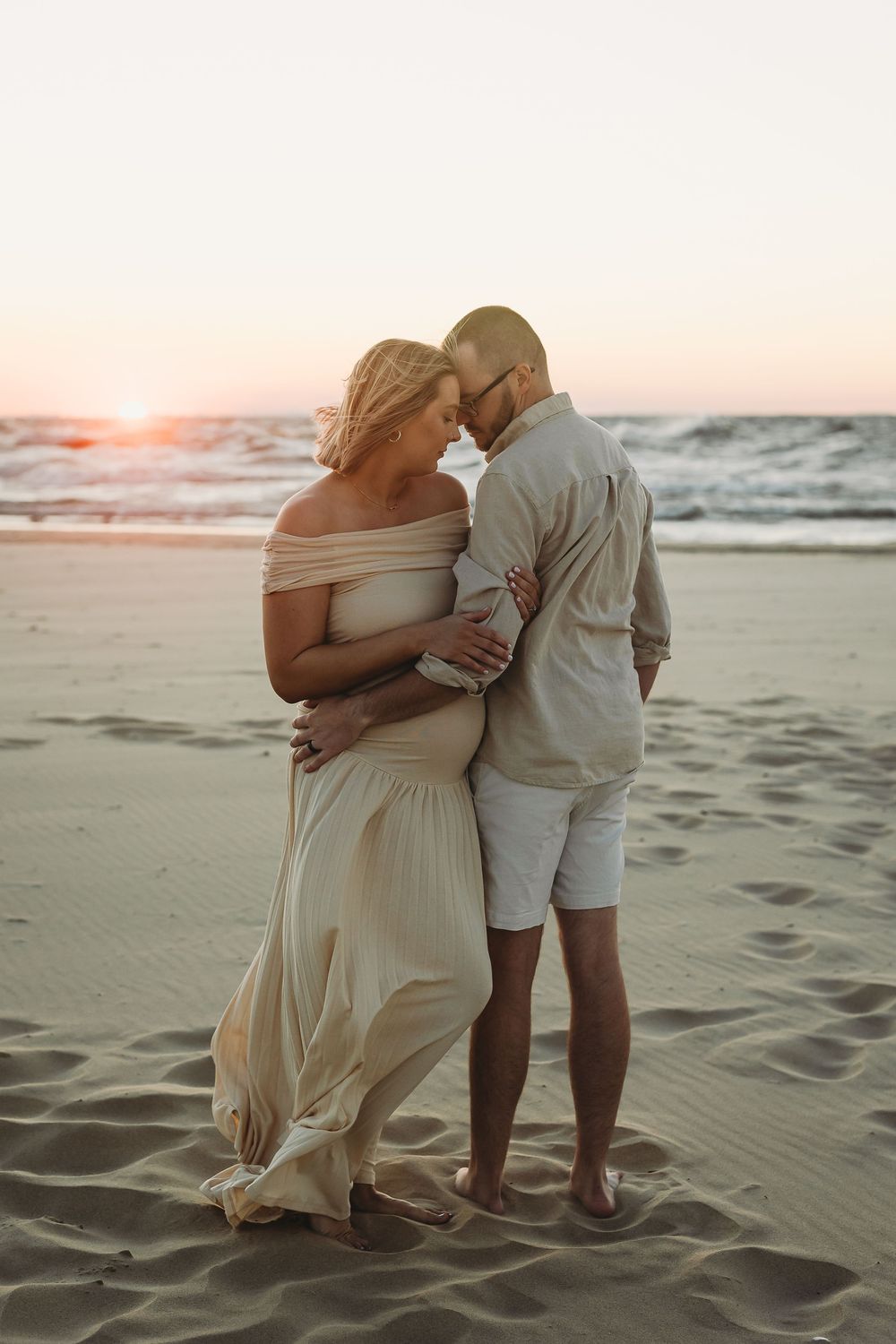 A couple embraces on a sandy beach at sunset in a series of romantic seaside photos.