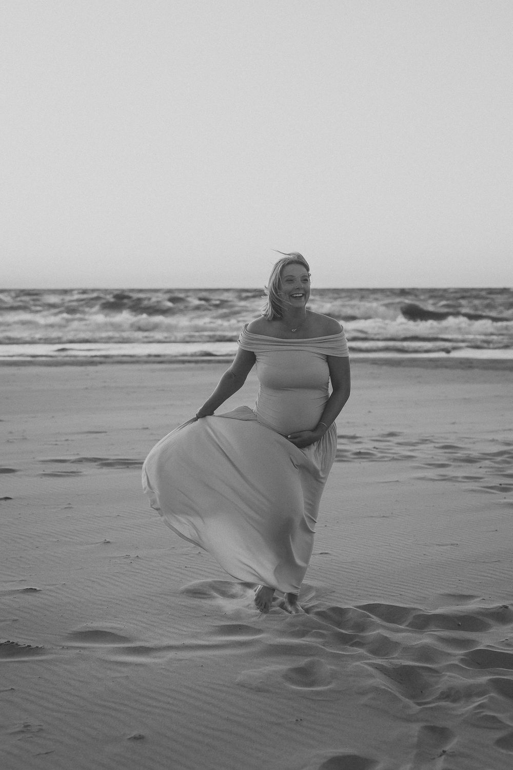 A series of black and white photos shows someone in light clothing crouching and interacting with the sand on a beach.