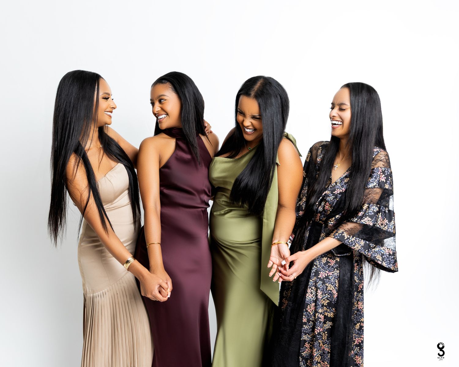 A group of women in formal dresses stand together smiling and laughing during a special occasion.