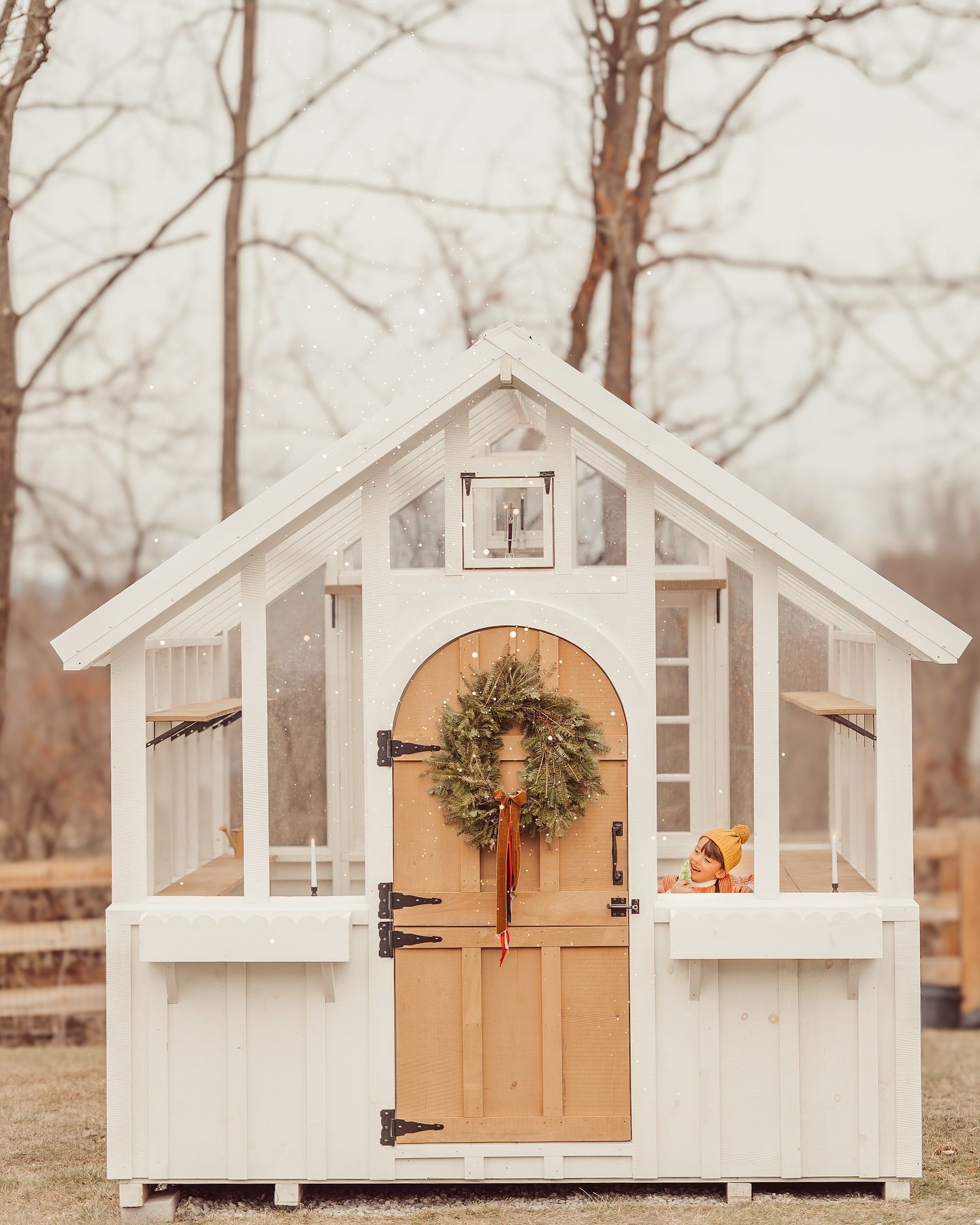 A charming white garden shed with windows and a wooden door decorated with a festive Christmas wreath.