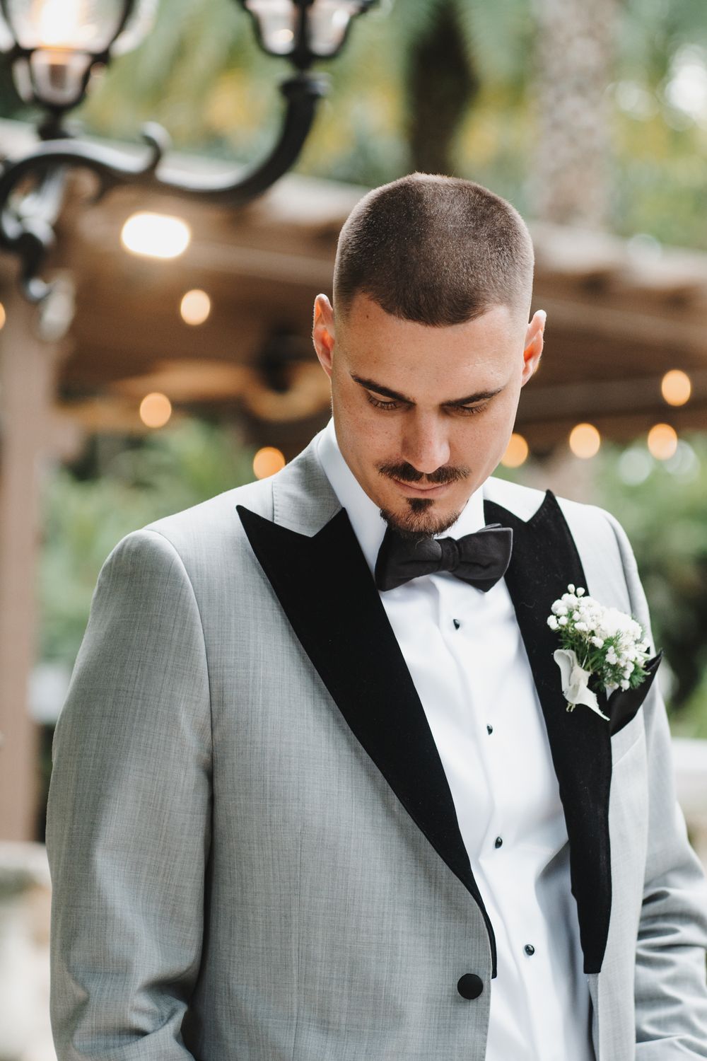 Close-up portrait of groom in light gray suit and black bow tie looking down during wedding ceremony.