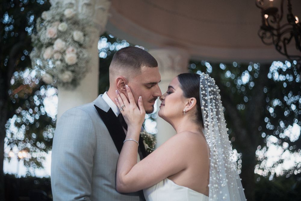 A bride and groom share a romantic kiss at their outdoor wedding ceremony, with floral decorations in the background.