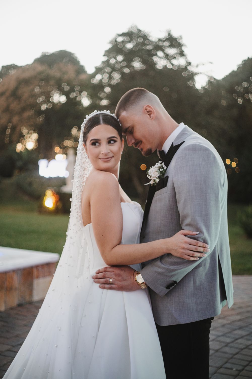 A romantic wedding couple embraces during golden hour sunset on a paved pathway.