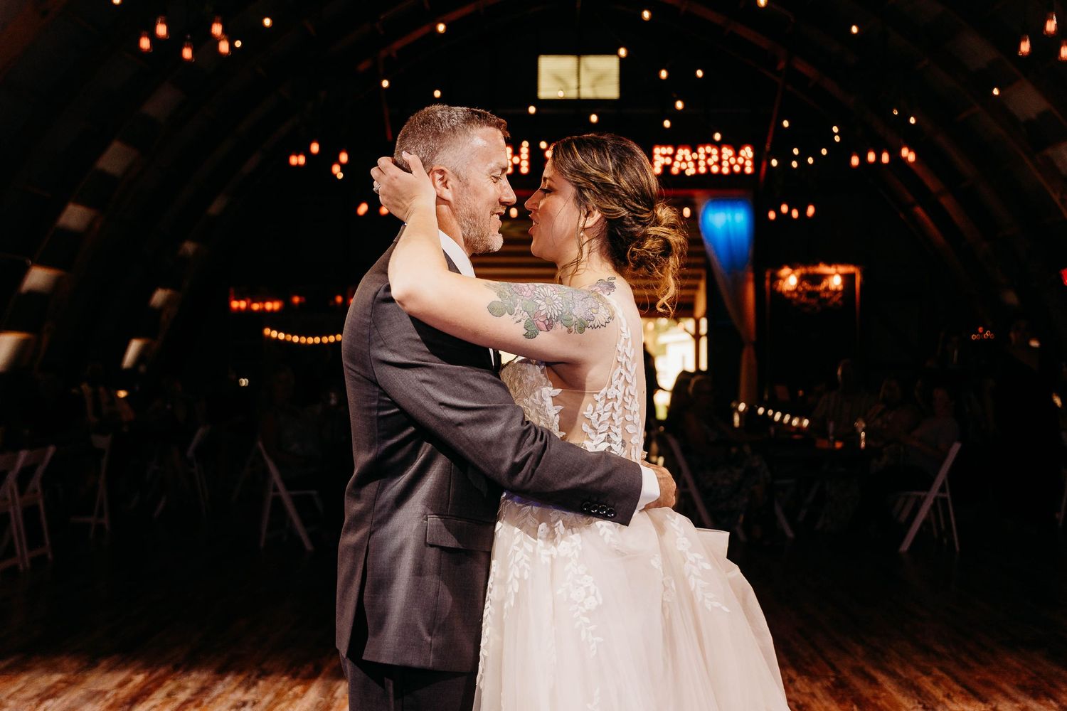 Romantic wedding couple shares their first dance on a dimly lit dance floor with warm glowing lights in the background.