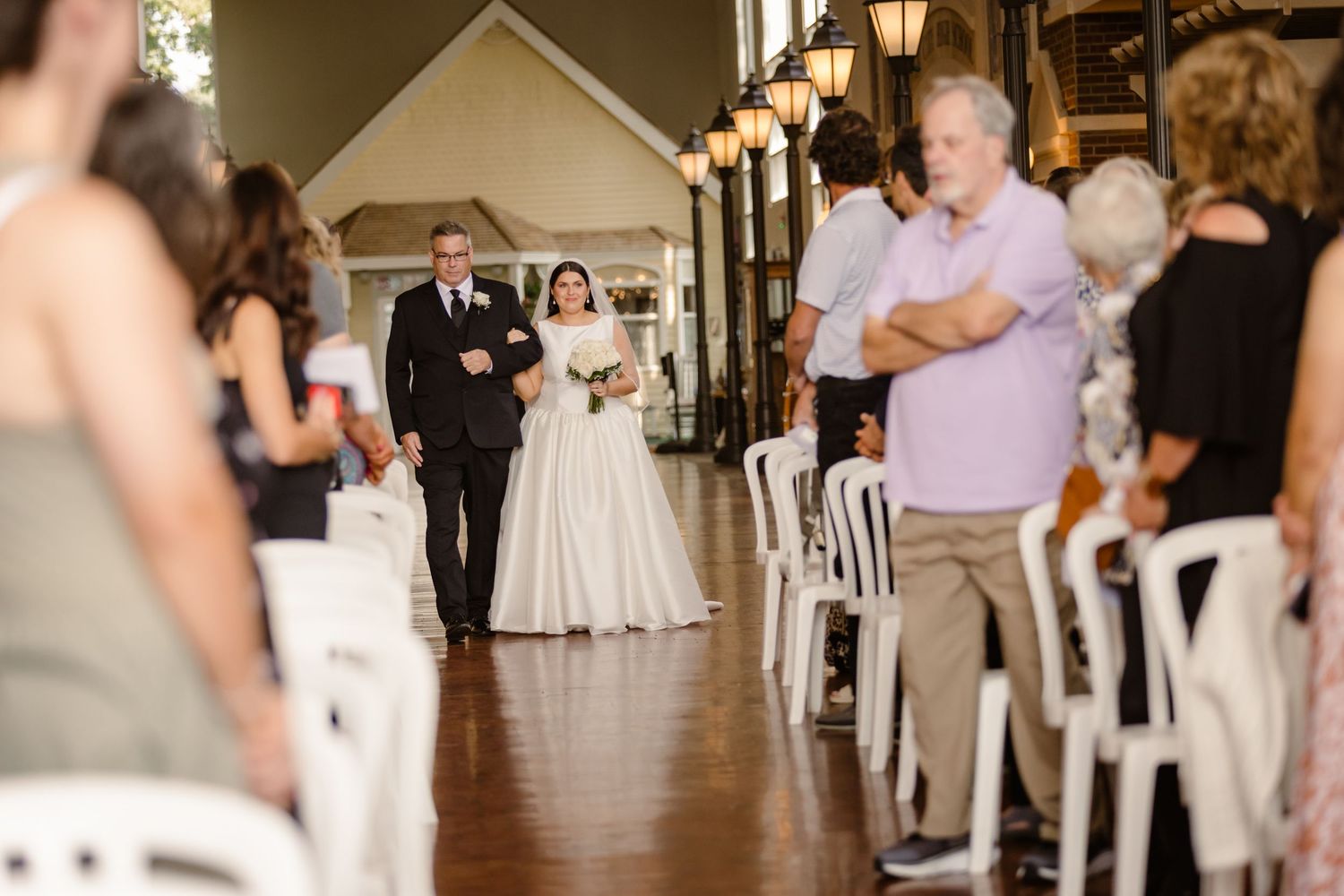 A traditional wedding ceremony processional with the bride in a white gown walking down the aisle with guests looking on.