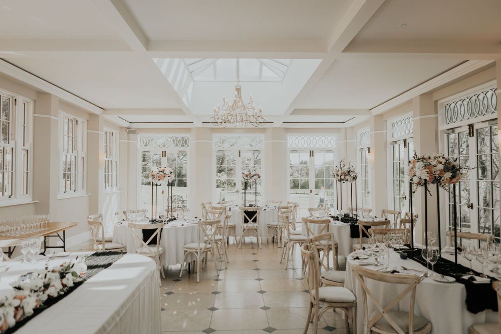 Elegant bright wedding reception room with chandelier, tall floral centerpieces, and black and white decor.