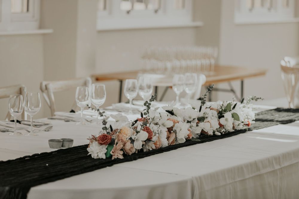 Wedding head table decorated with a lush floral runner of white and blush roses on black fabric.