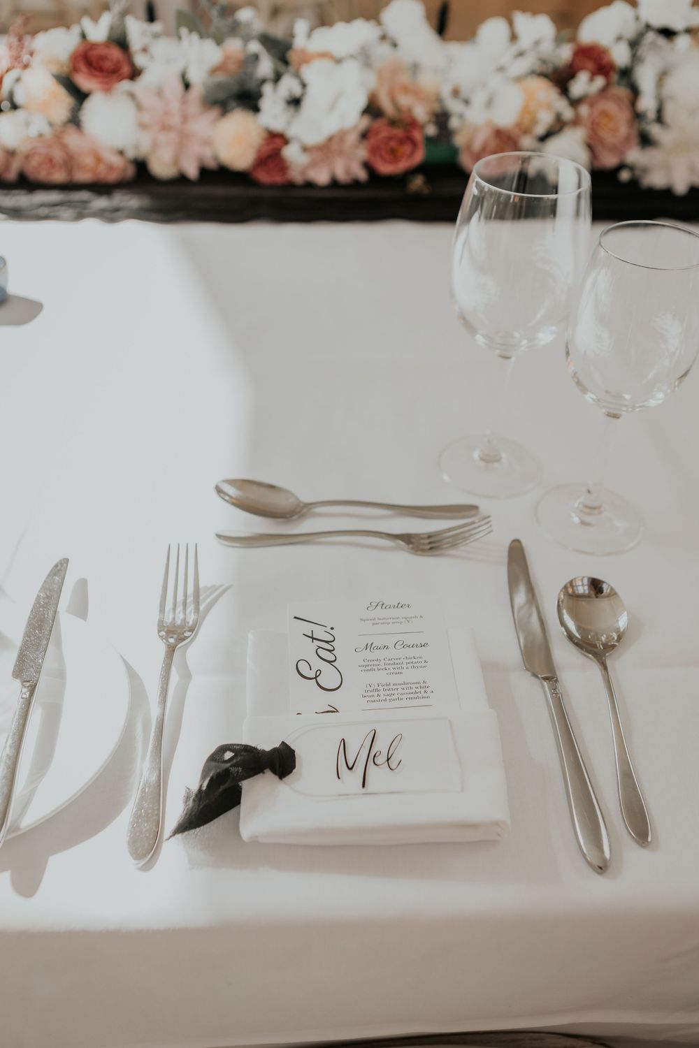 Wedding place setting with white napkin, silver cutlery, wine glass, and personalized menu card for Mel.