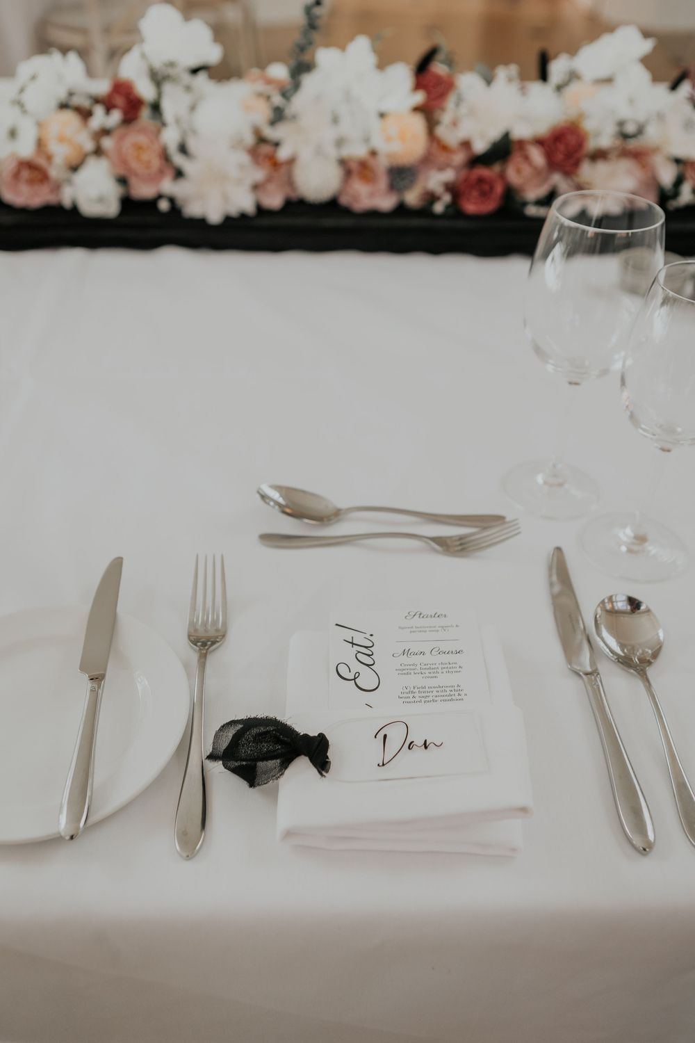 Elegant wedding place setting with white napkin, silver cutlery, wine glass, and personalized menu for Dan.