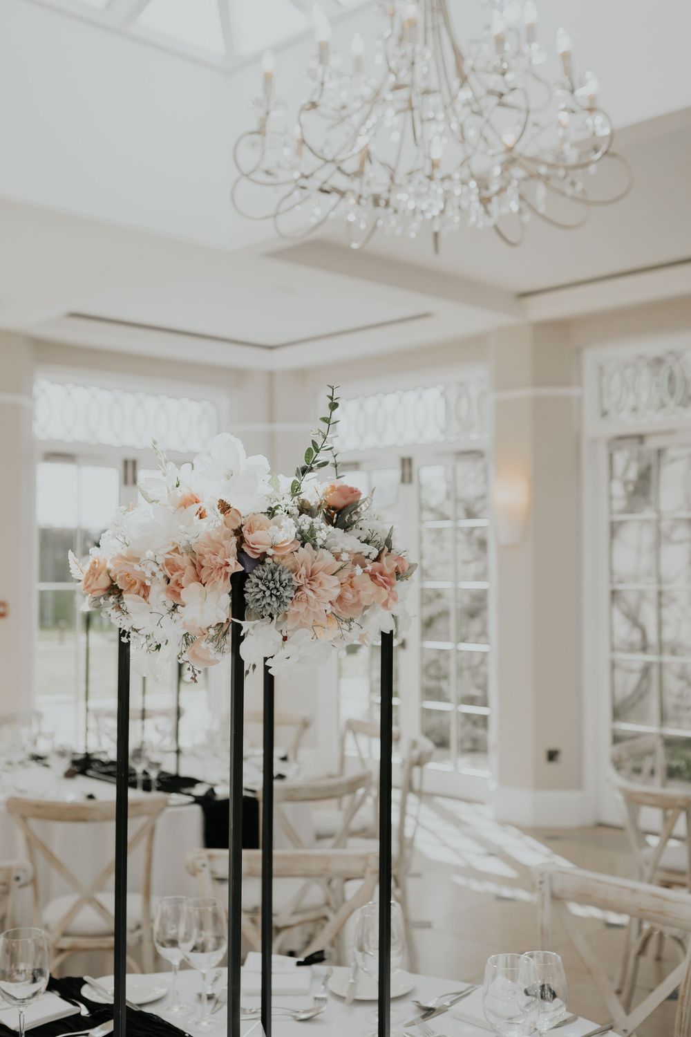 Tall black candelabra with blush and white floral arrangement in a bright elegant wedding reception room.