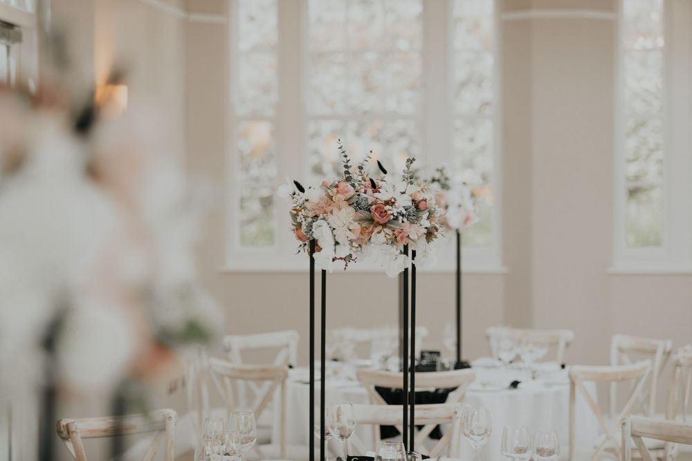 Elevated black stand with blush and white floral centerpiece in a bright white wedding reception venue.